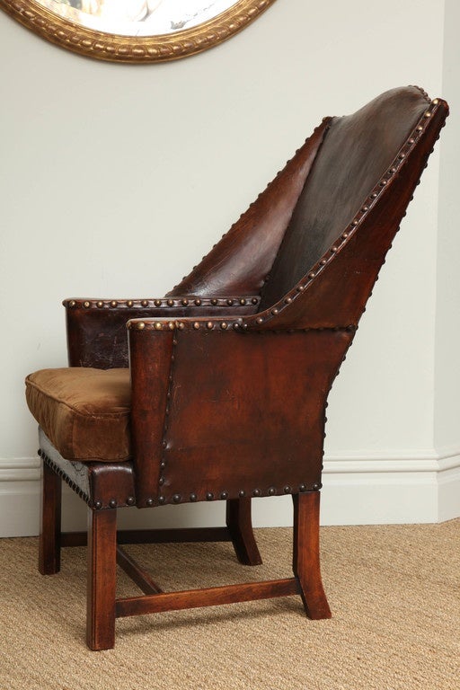 Stylish late 19th century English studded leather wingchair of extremely quirky design, the back with dramatic rake and gently outswept wings, terminating in scrolled arms with convenient flat surface for drinks glass, on beaded legs with gracefully