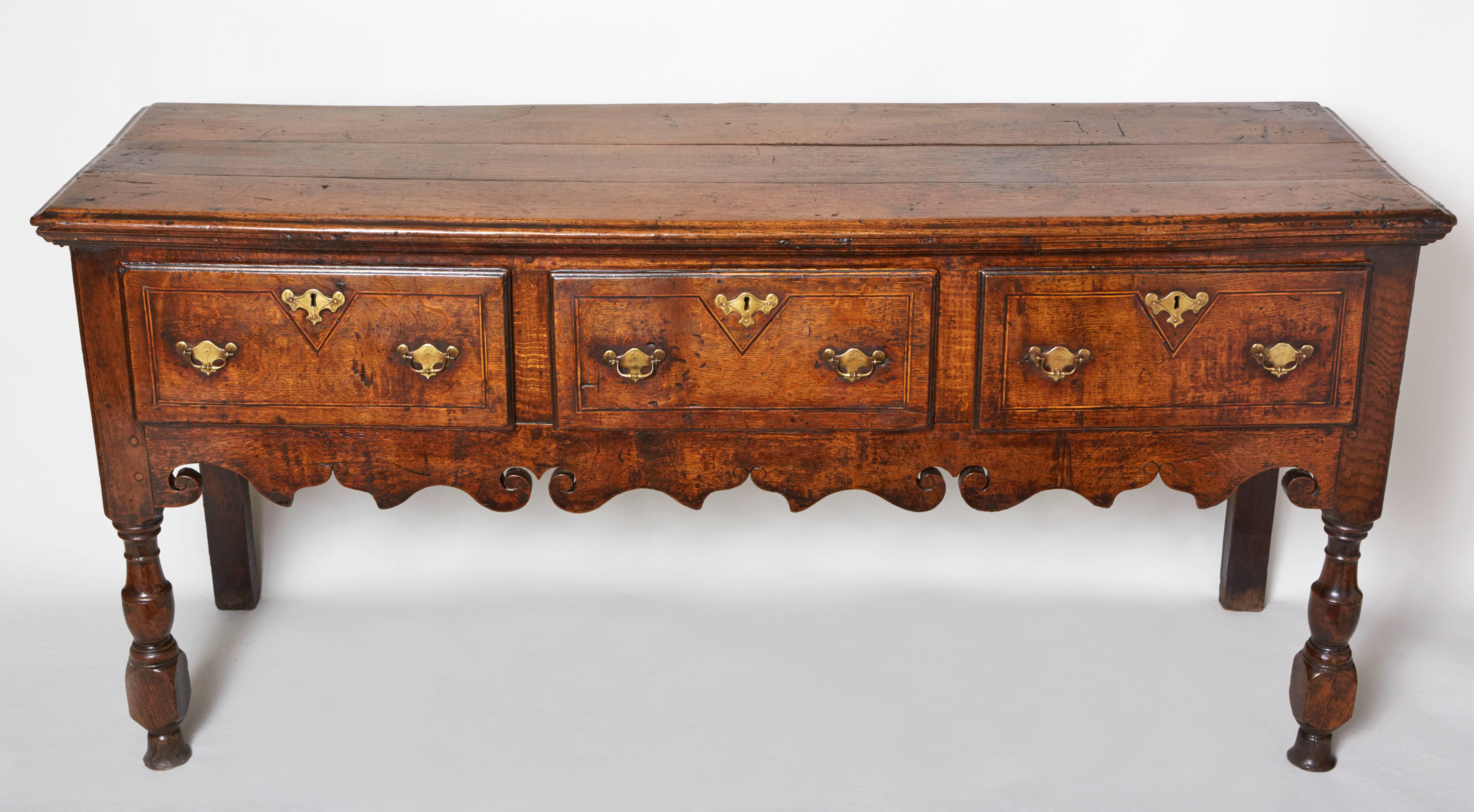 A fine early 18th century English oak low dresser, having a molded top over three inlaid drawers over lovely scalloped apron with whale's tail and cupid bow scalloping, standing on boldly turned legs, the whole possessing exceptionally rich color