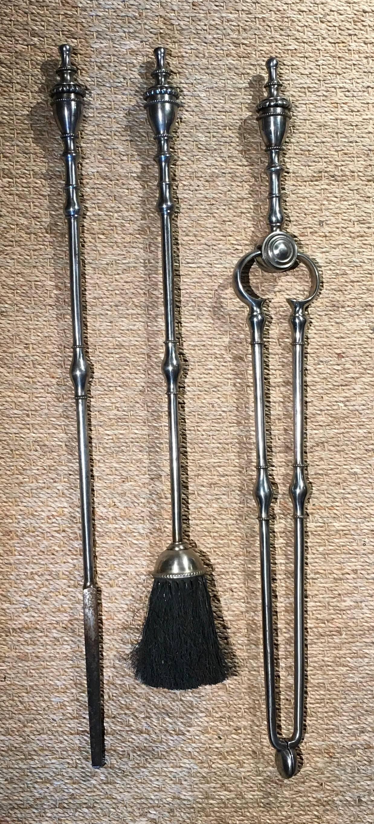 Very fine set of late 19th century English steel fire tools comprising a poker, tongs and hearth brush having bold urn handles, the shafts with ringed bulbous collar and the whole in good polished gun metal surface.