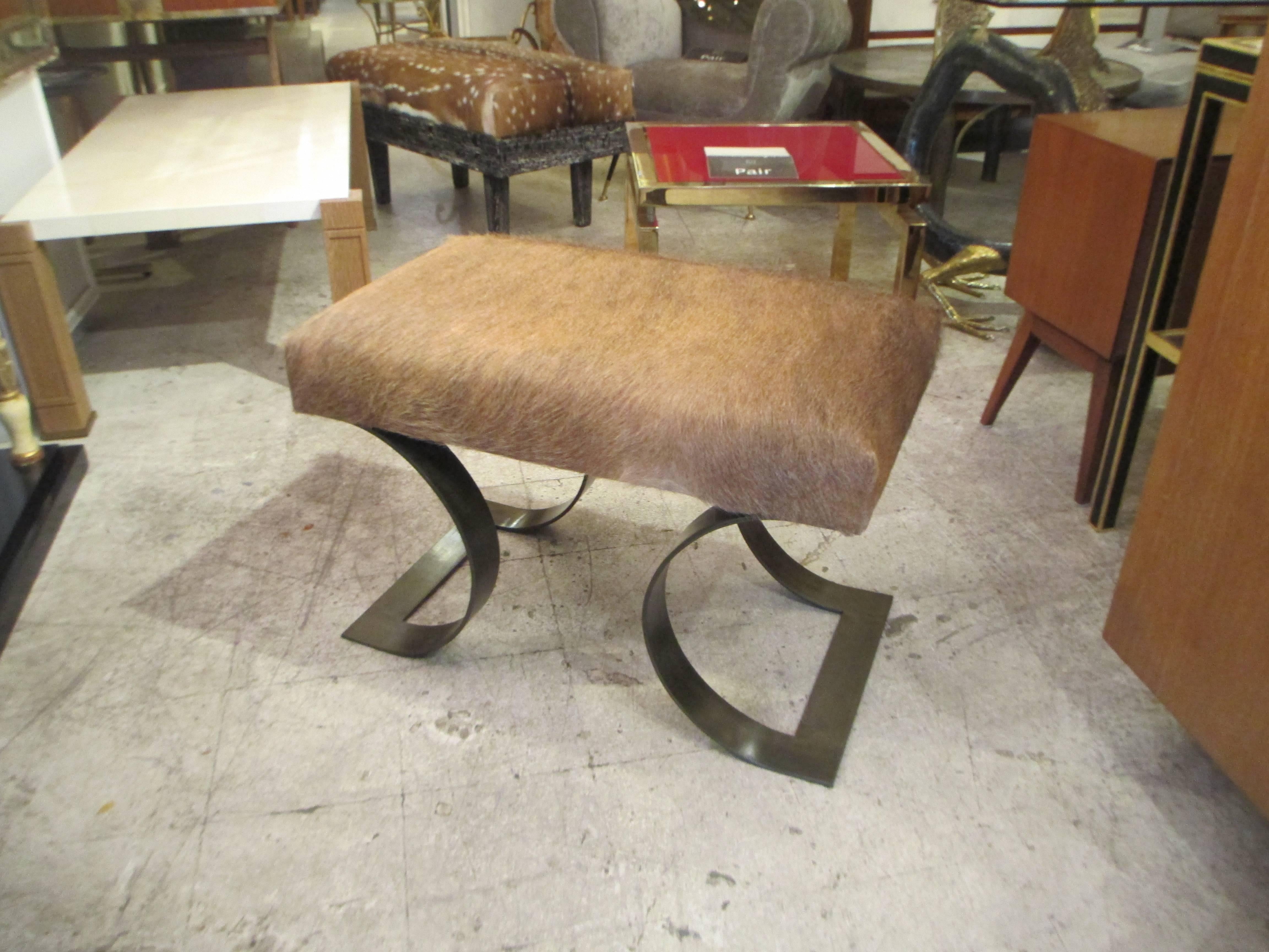 A pair of sculptural Mid-Century Modern benches upholstered in cattle hide on a polished iron base.