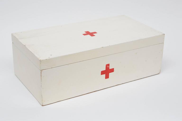 This well-made pine box has brass piano hinges with brass screws. The box is white with a hand-painted red cross emblem on the top and front.