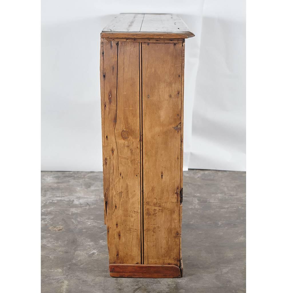 This English or possibly Irish pine base has two drawers over two doors. It stands on a plinth base. It shows wear and some old repairs, but stands strong for more use. It is narrow and can work in a special place.
  