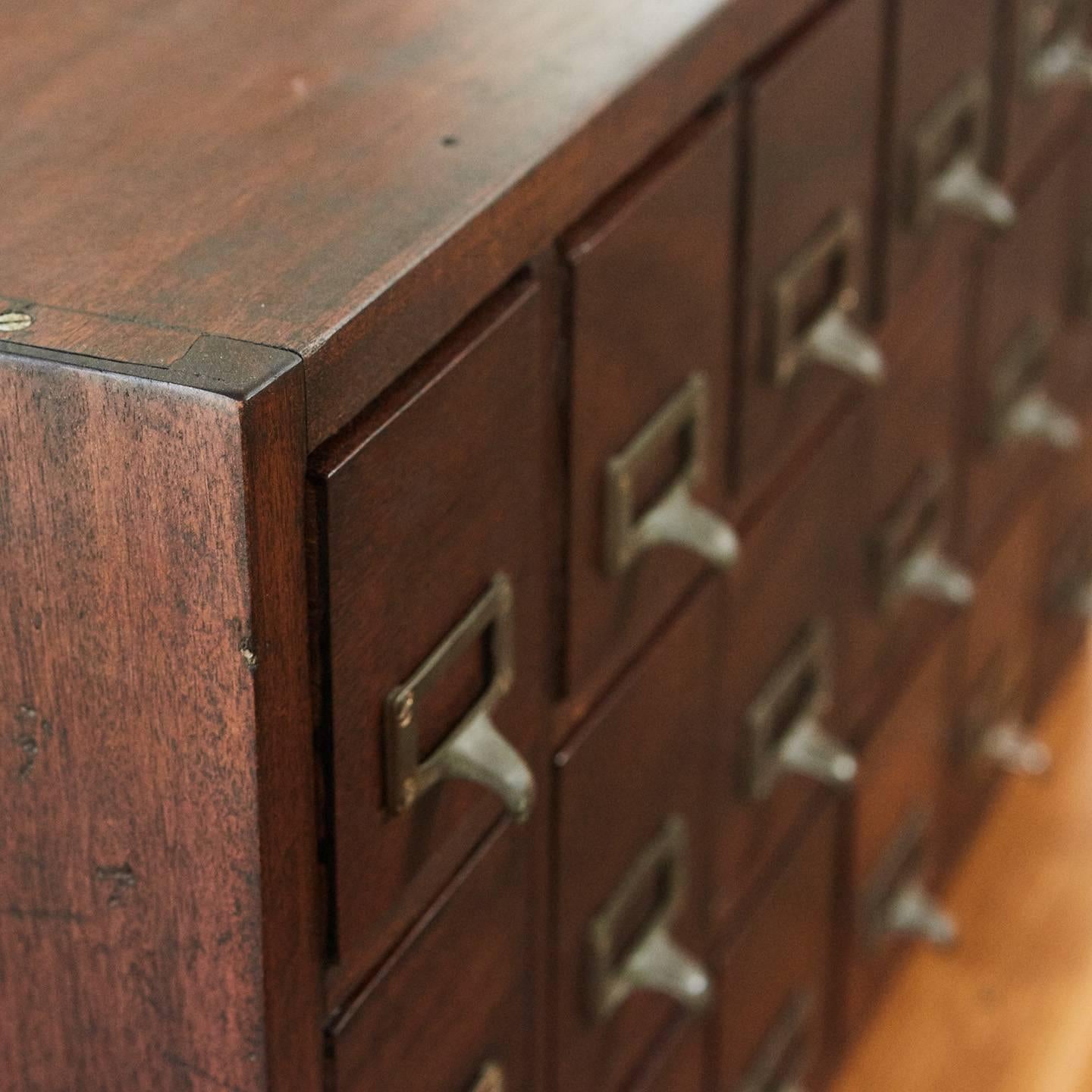 This wooden, 18-drawer card catalog cabinet has brass tab pull handles and label frames on each drawer. This piece could have been used in a library or office at the turn of the 20th century. The piece has a great look and is well suited for a