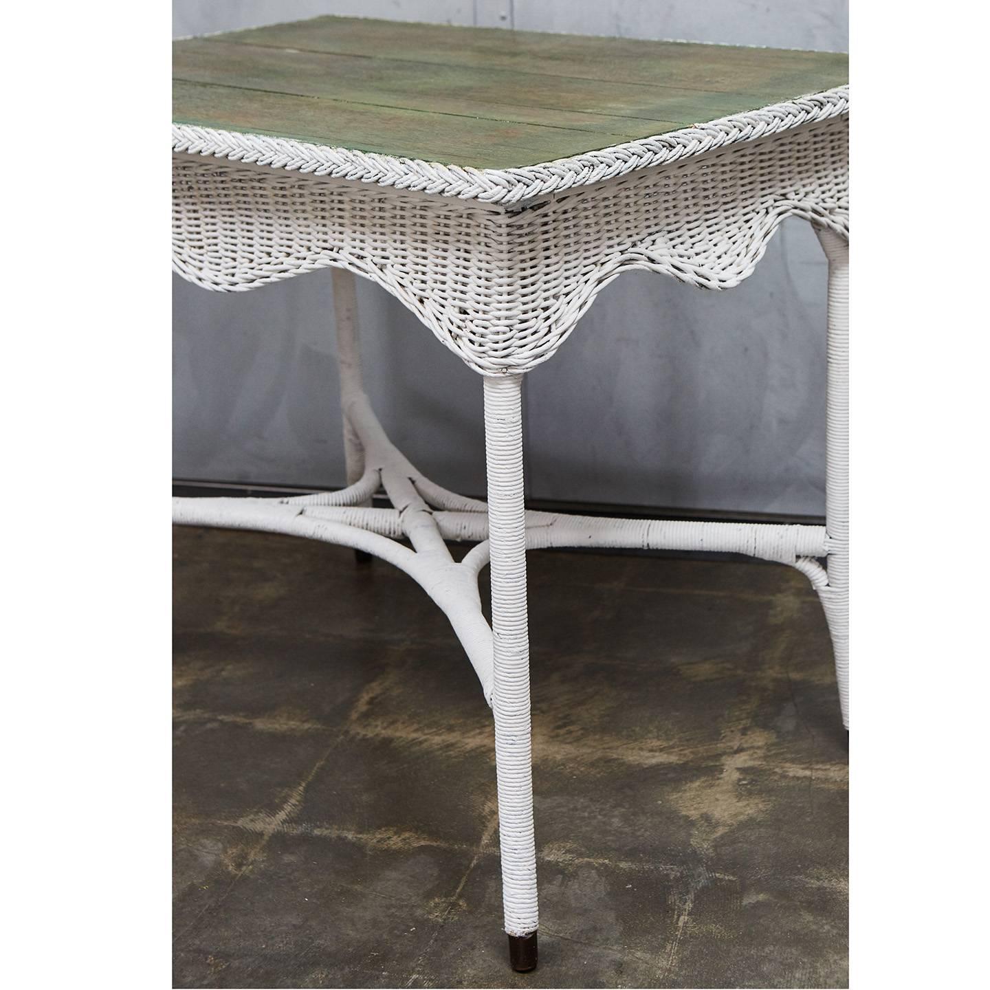 This nice wicker table has a veneer top that has remnants of paint leaving a nice jade green finish. This charming piece also has a scalloped skirt and splayed feet with metal tips.