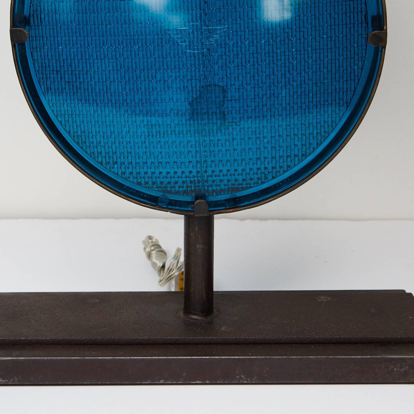 This lamp is made from two railroad light lenses set in a circular steel frame on a rectangular base. The lenses are from a railroad light from the first half of the 20th century. The convex blue lenses have are textured on one side with smooth