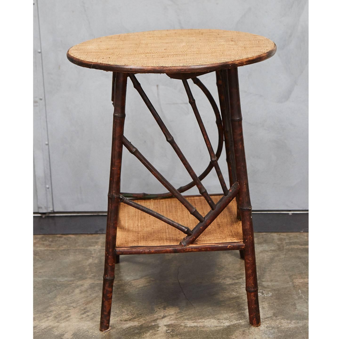 This interesting bamboo table with a circular top has wonderful bentwood elements that create web like supports between the top and shelf. The table has an open side with a turned finial and nicely angled feet. The table has newly installed waxed