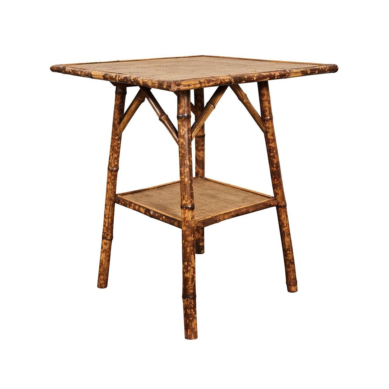 This nice square top English Victorian tiger bamboo table has angled supports and one shelf. The legs have been reinforced with wooden dowels for increased sturdiness. The surfaces have been newly re-done in waxed raffia matting. We have more of
