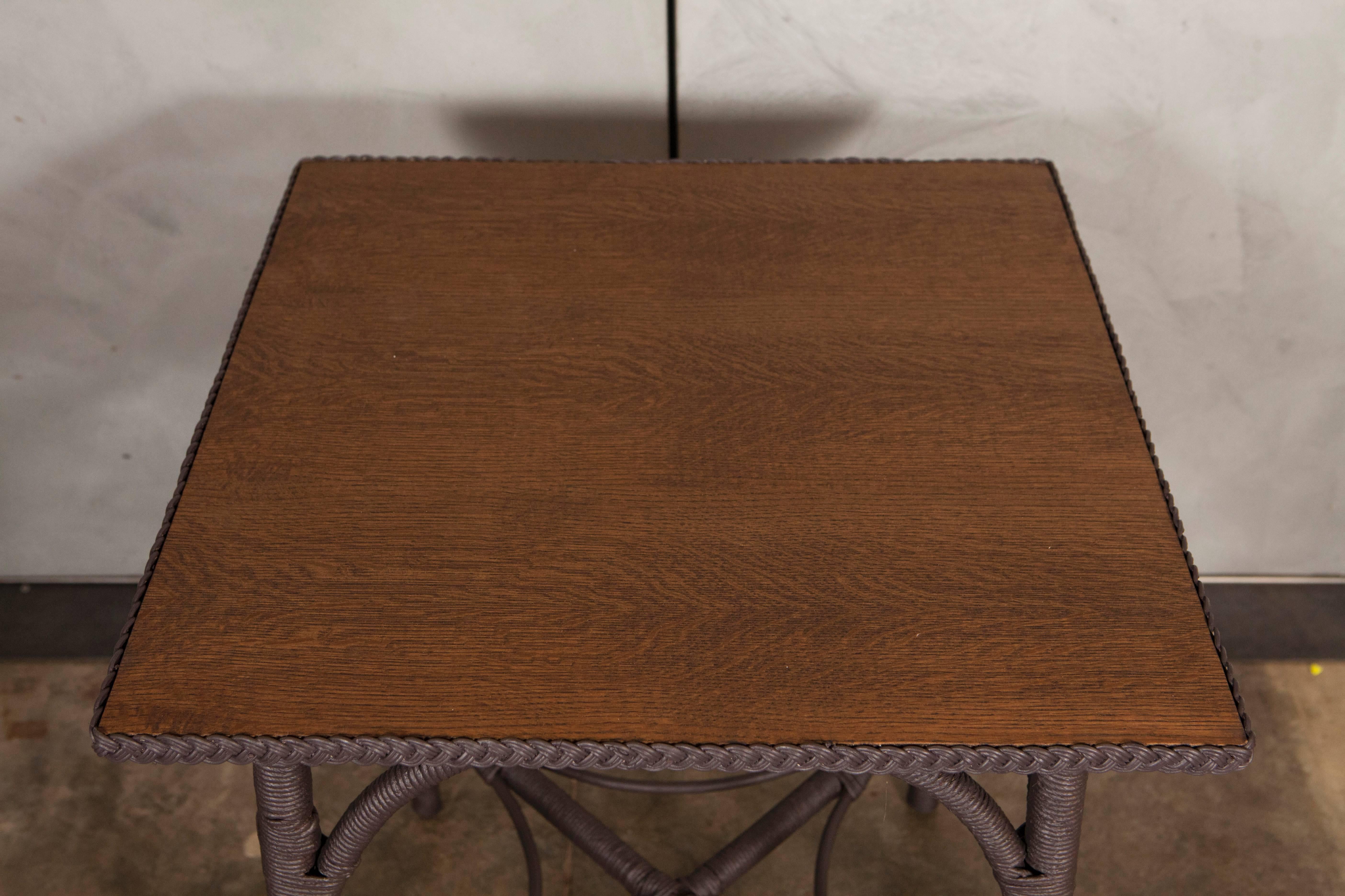 This small table with an oak veneer top is a beautiful example of Lloyd Loom Furniture made in the United States in the early part of the 20th century. Lloyd Loom furniture was the invention of American, Marshall B. Lloyd who developed a method to