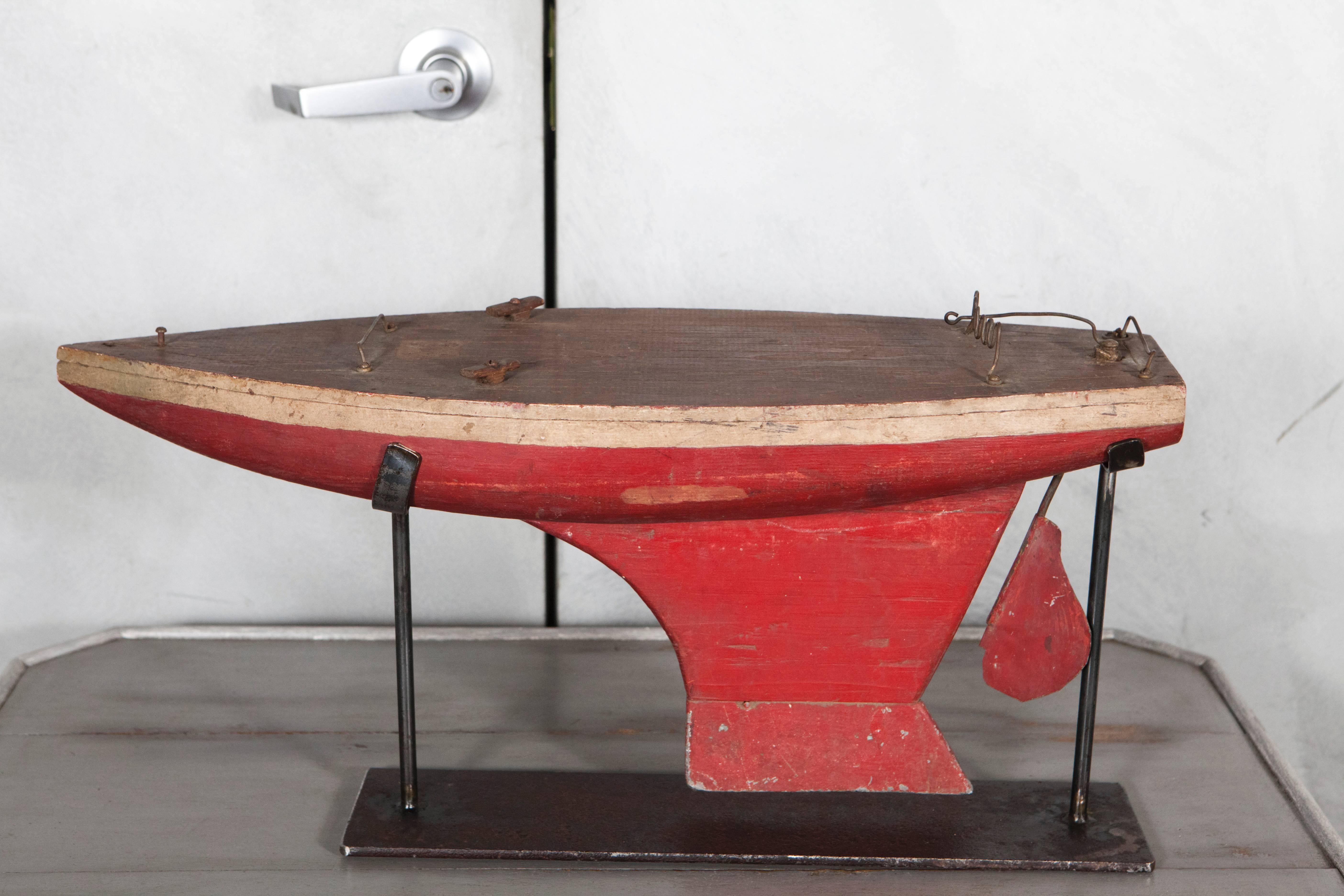 This nice vintage pond boat hull has a wood deck with various metal elements that relate to the rudder. The body is painted in red and white with a nice patina showing that this boat was a vessel that took many a voyage. The piece has a custom
