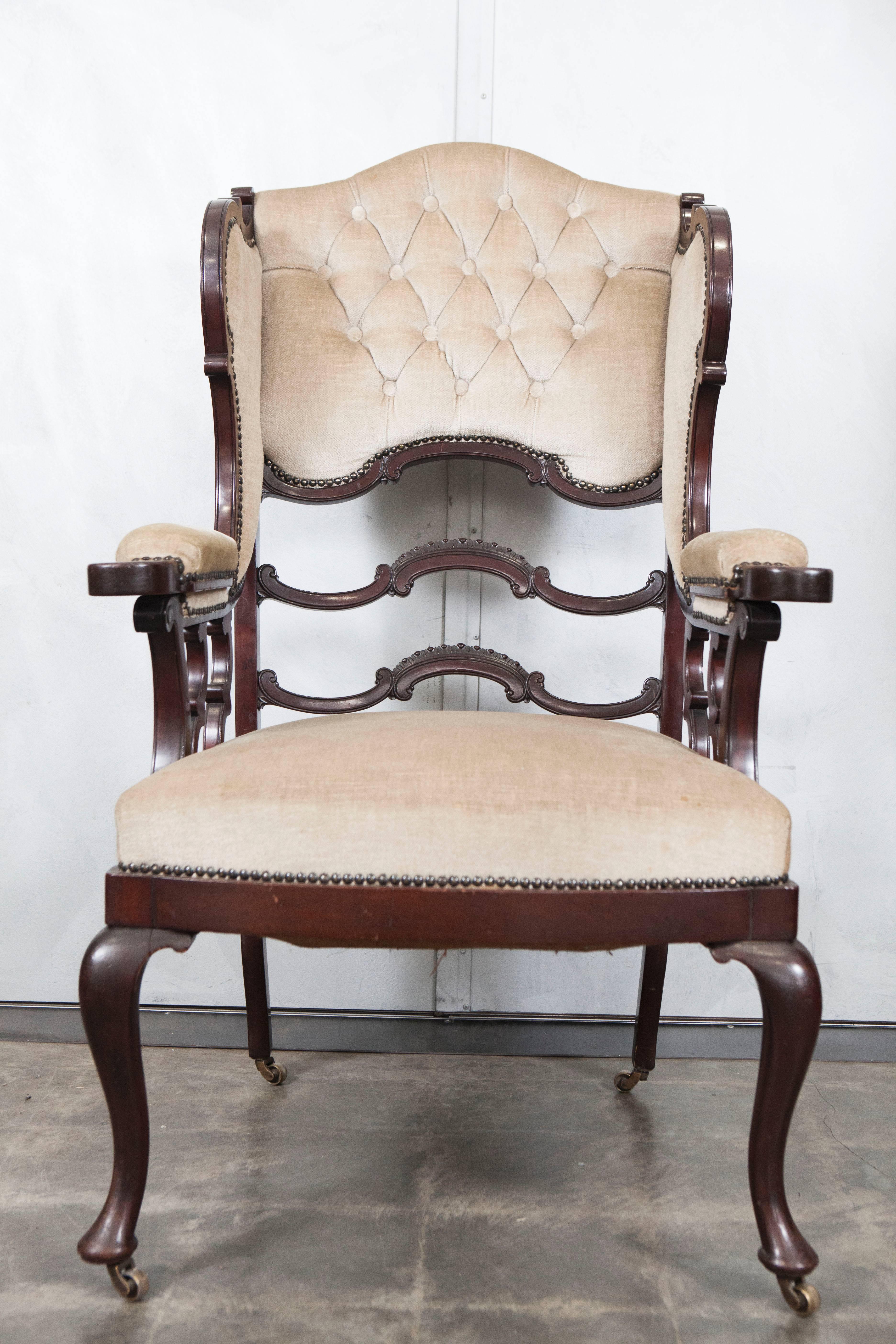 This wingback armchair is likely from late Victorian age with indications of period craftsmanship and signs of age. It's style is something of a wonder with interesting open back and open-arm design elements that seem to be an individual designer's
