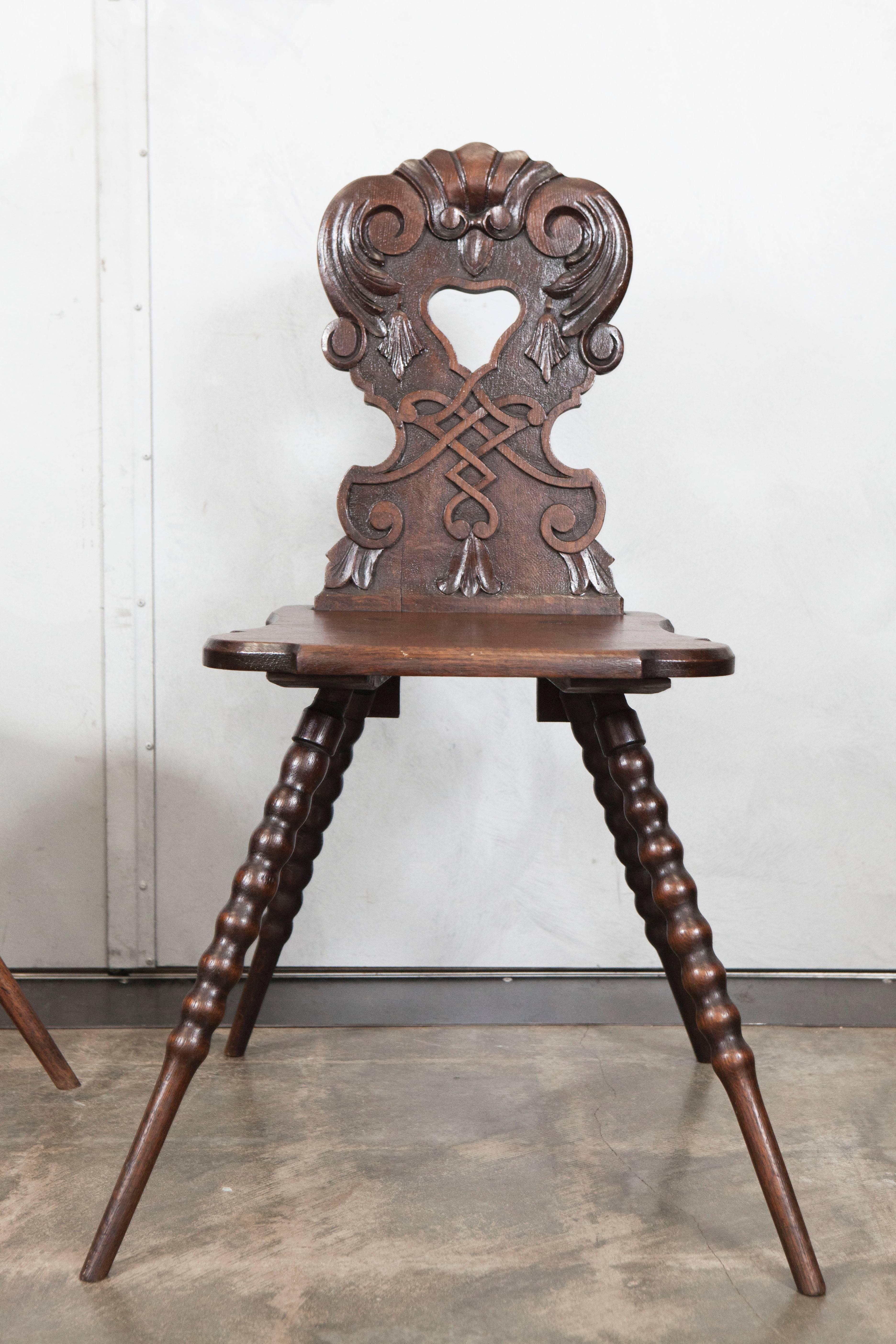 A nice pair of carved, pierced oak hall chairs with turned legs that point outward in the Tyrolean style.