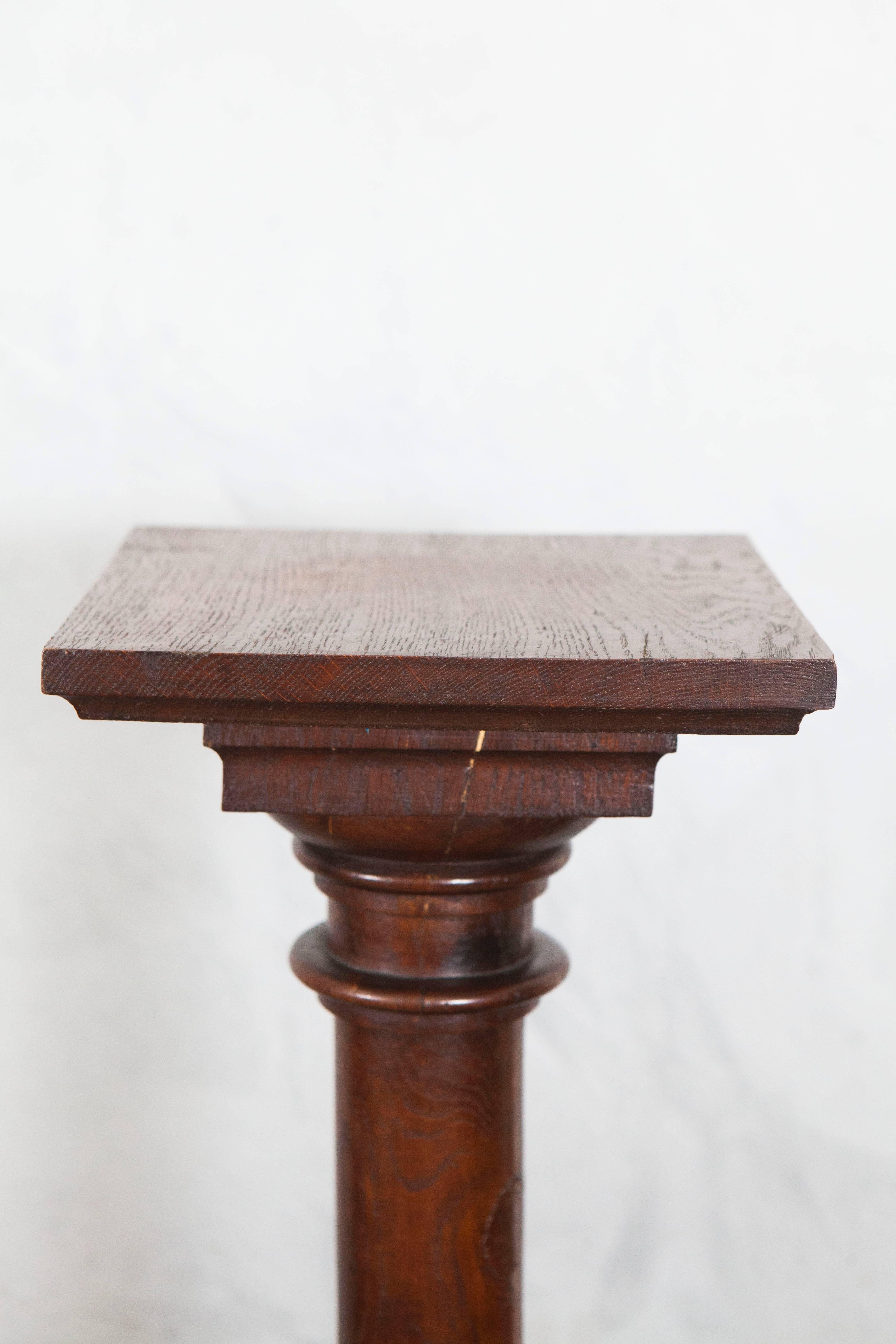 This attractive oak pedestal has a square top with nice delicate turned layers, rounded carved center piece and a stepped square base.