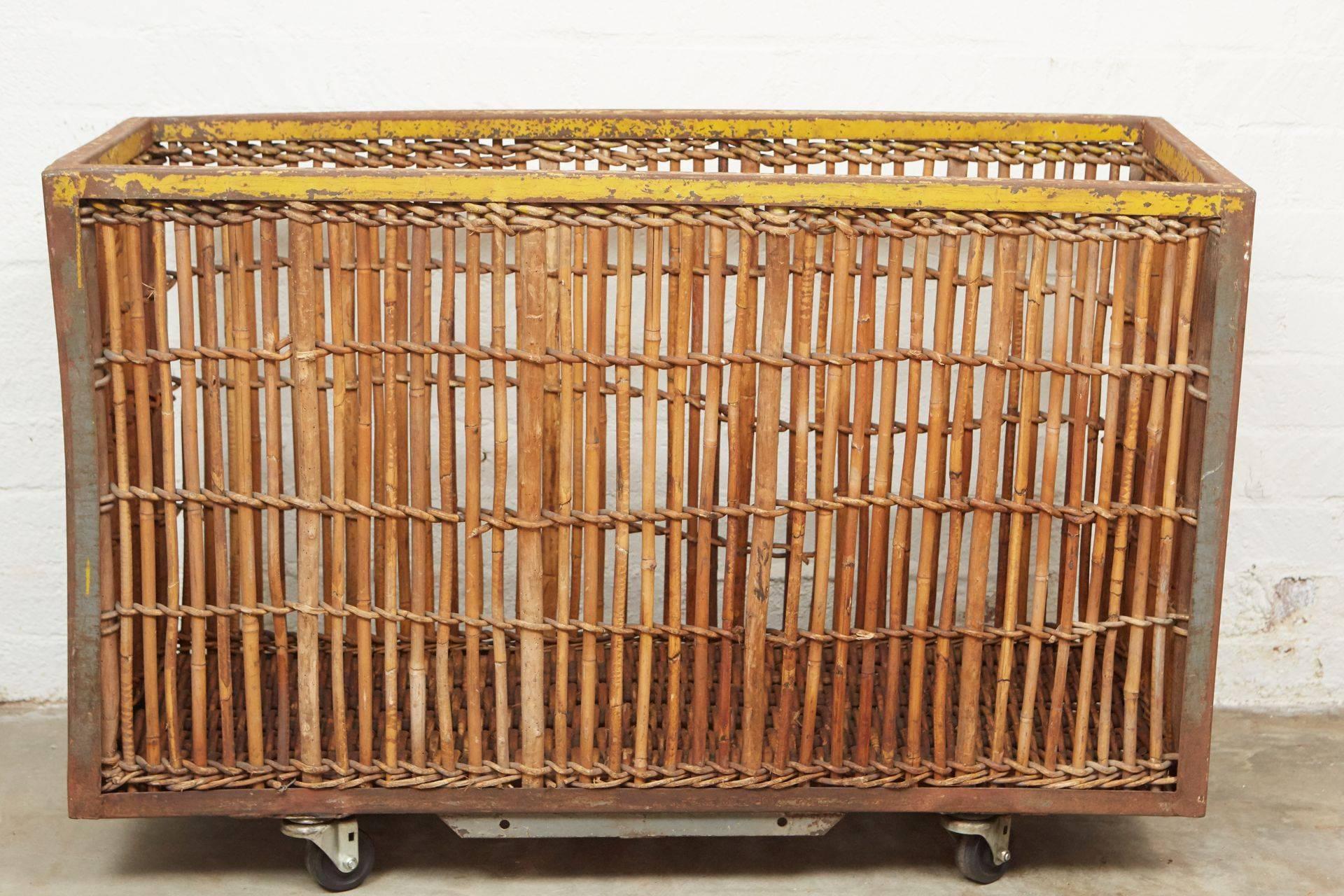 This great piece, circa 1900, has bamboo and wood woven sides and bottom on an iron frame with remnants of yellow and black paint. There is a hand-lettered tag on one side of the cart as well. The cart is sits on casters with wheels. Functional and
