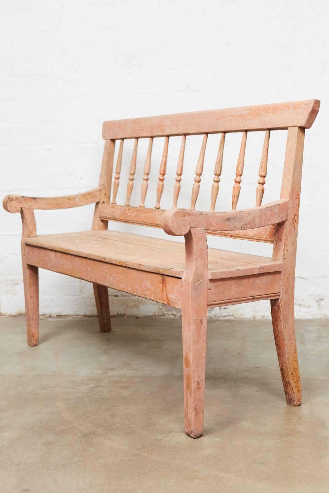 Spindle back bench for two with two arms on four square tapered legs, shaped arms and top rail. Once painted pinkish orange, surface shows fading, rubbing, losses as is usual with a distressed finish.
