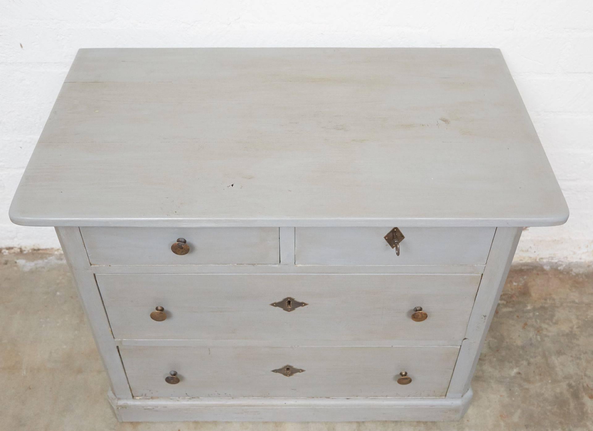 This grey painted chest of drawers has brass knobs and escutcheons. The top right drawer has a lock and key and can be used for your valuables. The chest is a good size for a bedside piece. 

 