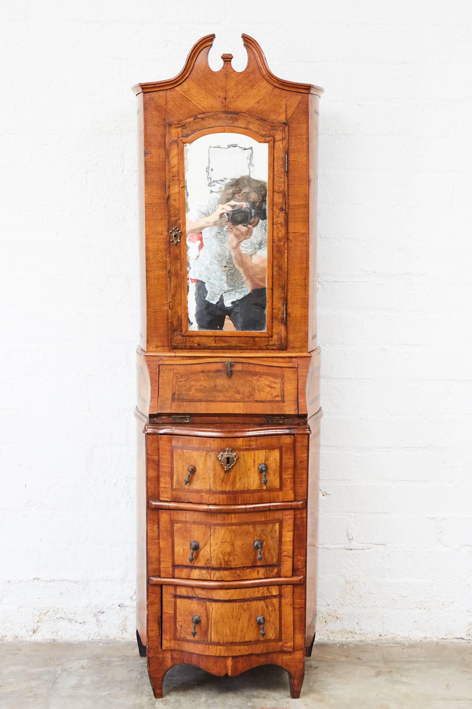 This 18th century secretary has serpentine base, desk and an upper cabinet with an original mirrored door. The piece is made with walnut veneer which has extensive repairs that act as documentation to the centuries of wear and use.