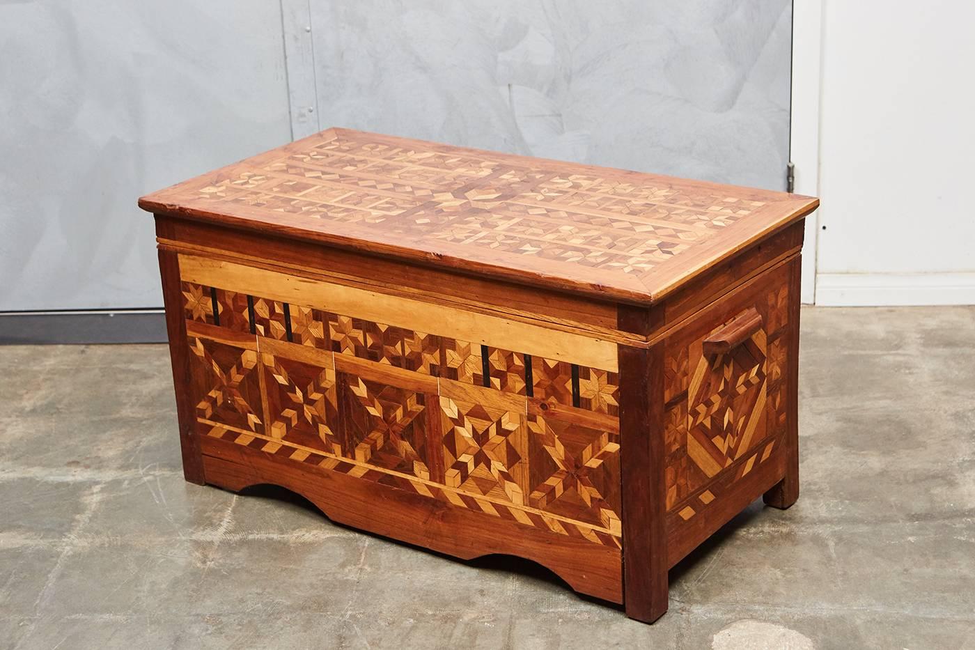 This American Folk Art trunk has wonderful inlaid patterned parquetry on all sides with a cedar interior. The trunk stands on for feet with a carved skirt and wooden handles.
   