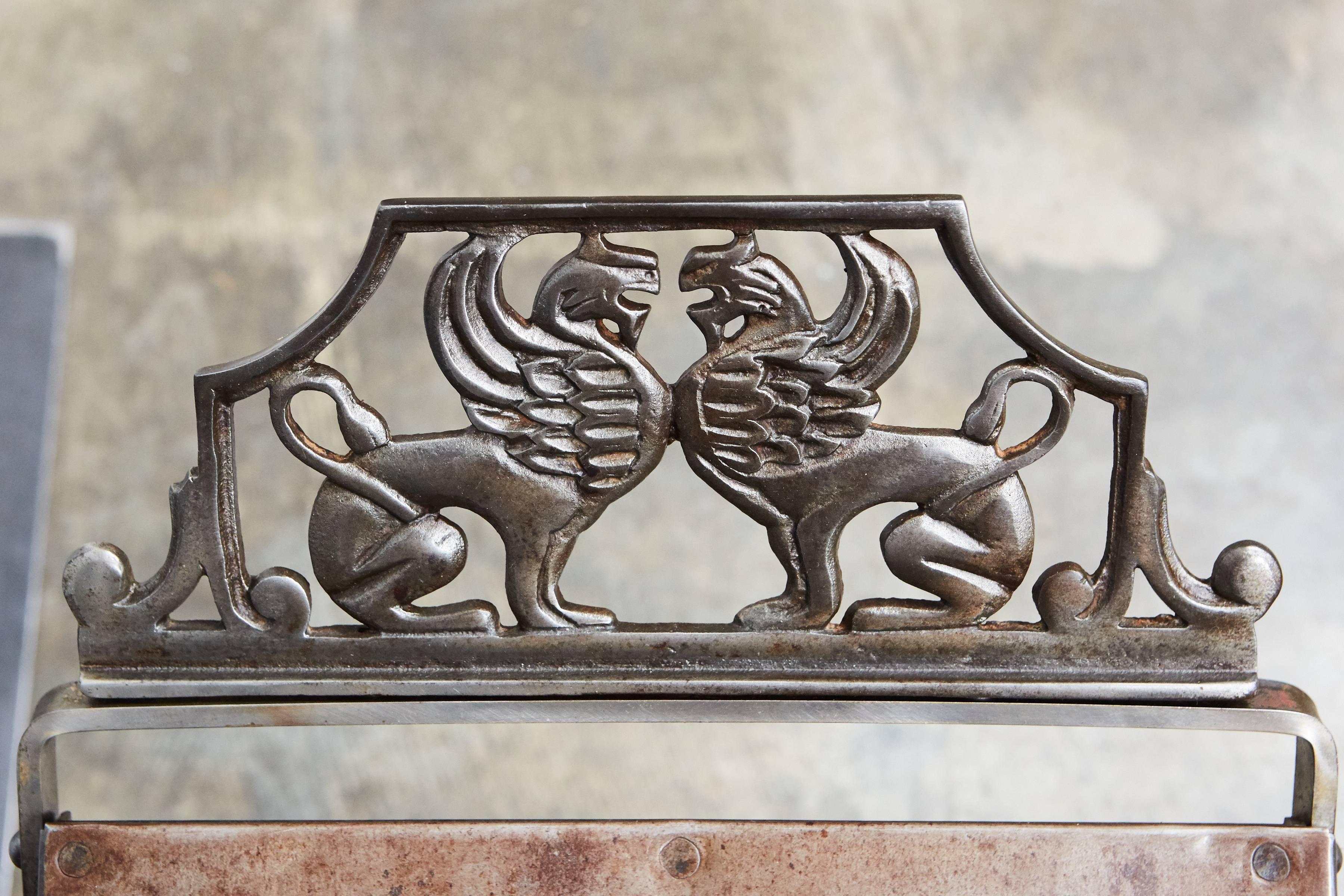 This lovely metal stool from the 1920s has two nicely articulated griffins on each side of a curved fixed seat. The four crossed legs have two stretchers with floral details. This piece has unique construction and design with a wonderfully rich