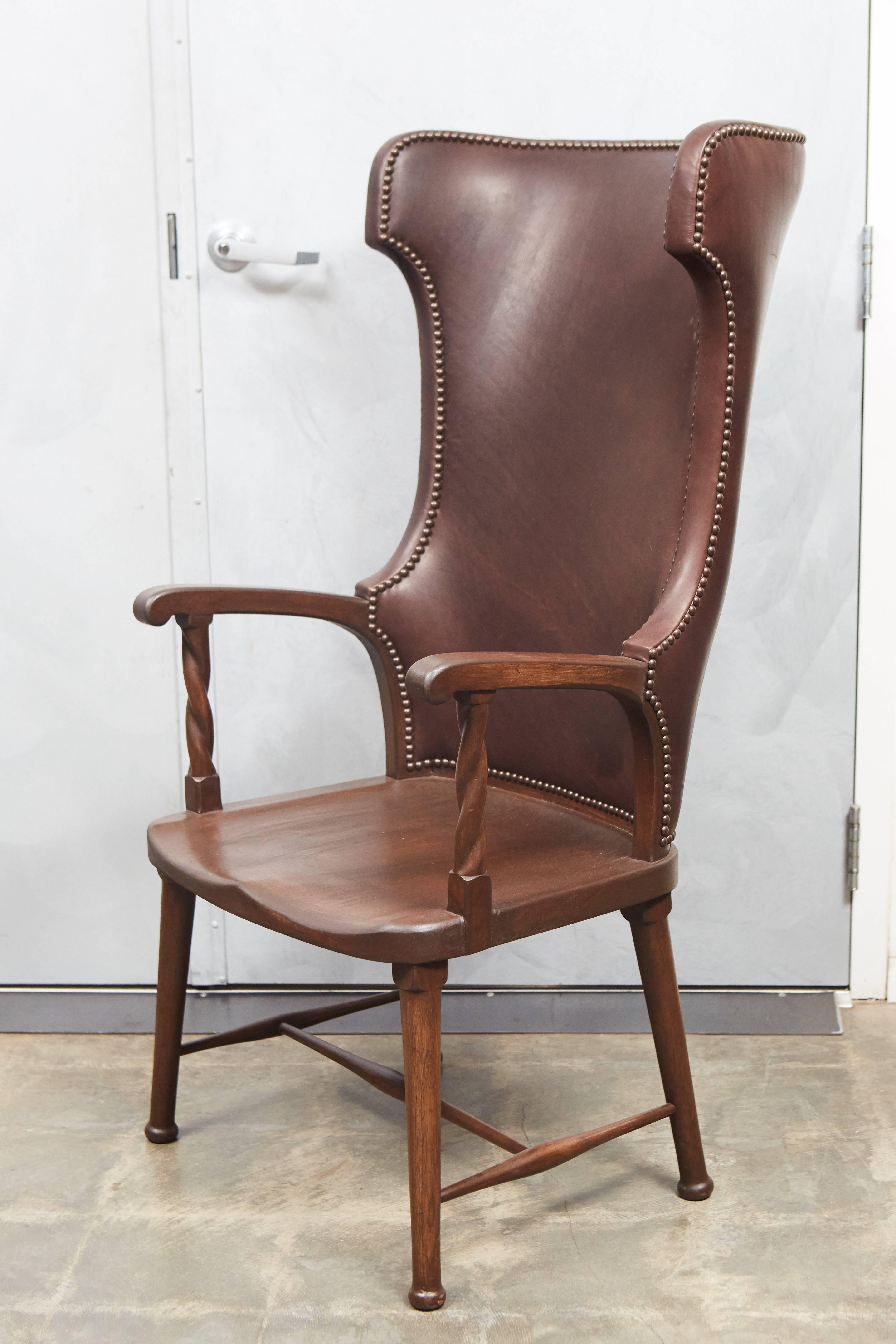 This high back armchair has a dynamic shape with an exaggerated tall back and nicely shaped wood arms and legs. This piece has been recently re-upholstered with a rich brown leather and large brass upholstery tacks that give the well crafted antique