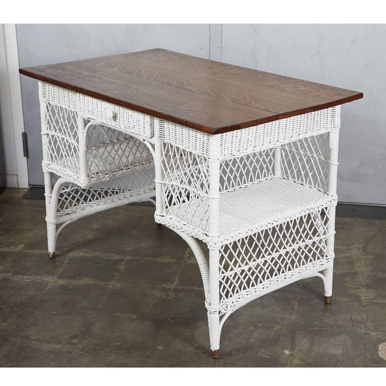 This wonderful example of wicker furniture from the 1920s is made of woven reed with a wood frame and oak desk surface. It has lattice patterned sides with side opening for two shelves. The piece has one drawer with a turned wood knob and the brass