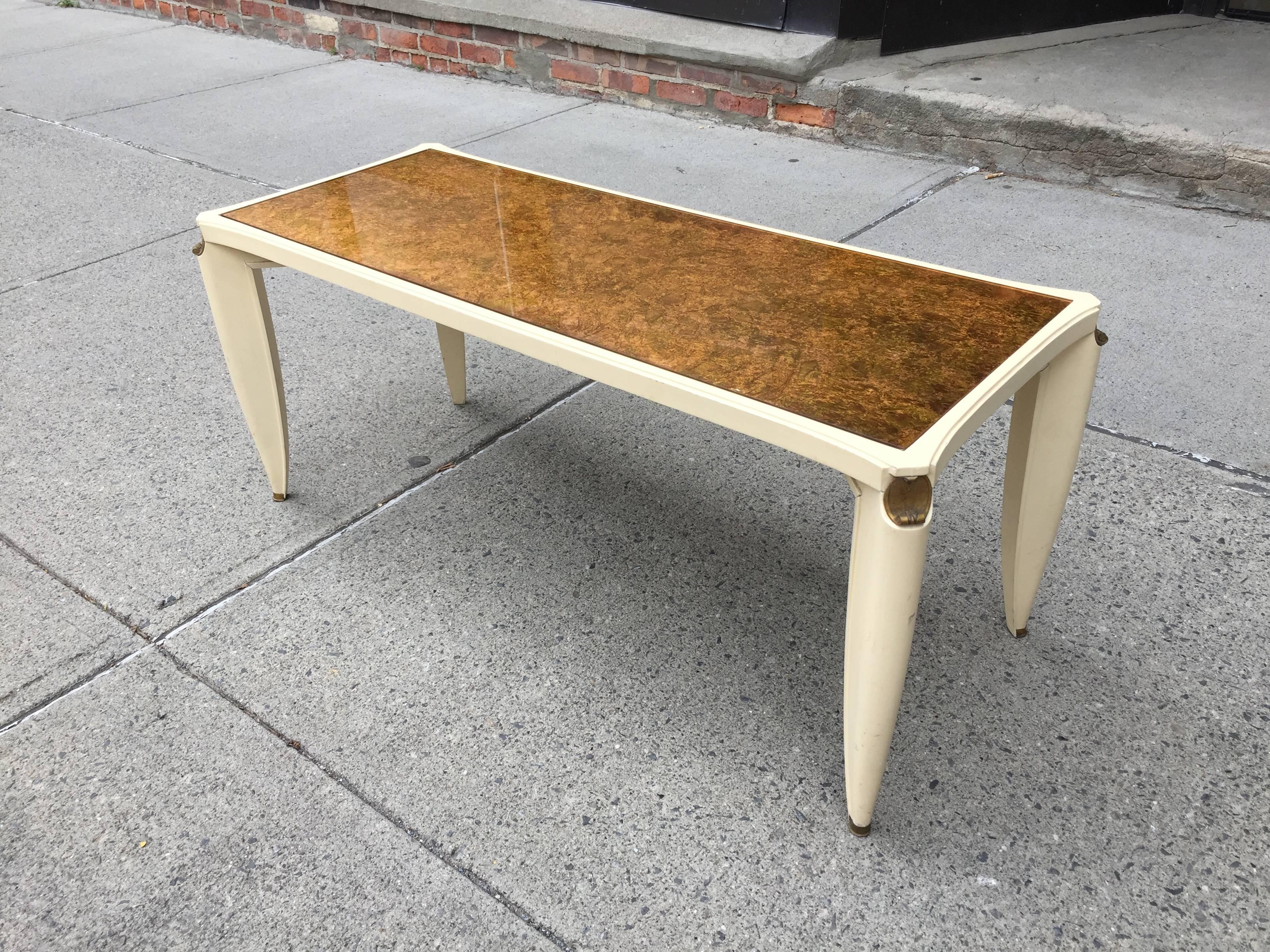 Cream-lacquered table with gilt metal sabots and gold and silver-leafed eglomisé glass top.