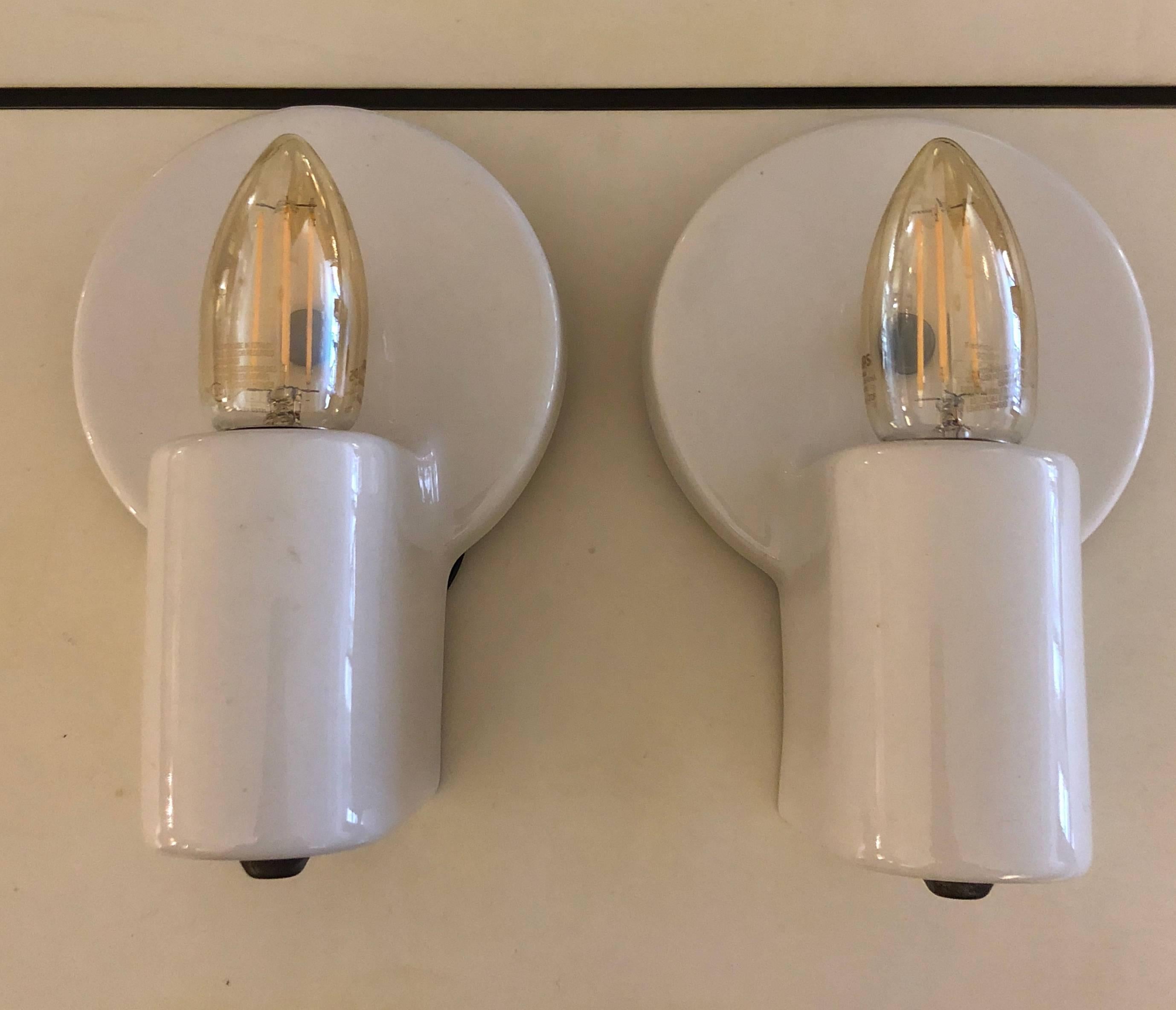 White porcelain wall lights designed by the great Swiss modernist architect. This pair is nicely minimalist, eschewing the usual pull chain, and embellished with the simplest brass tab hardware. For Pass & Seymour, USA, circa 1935