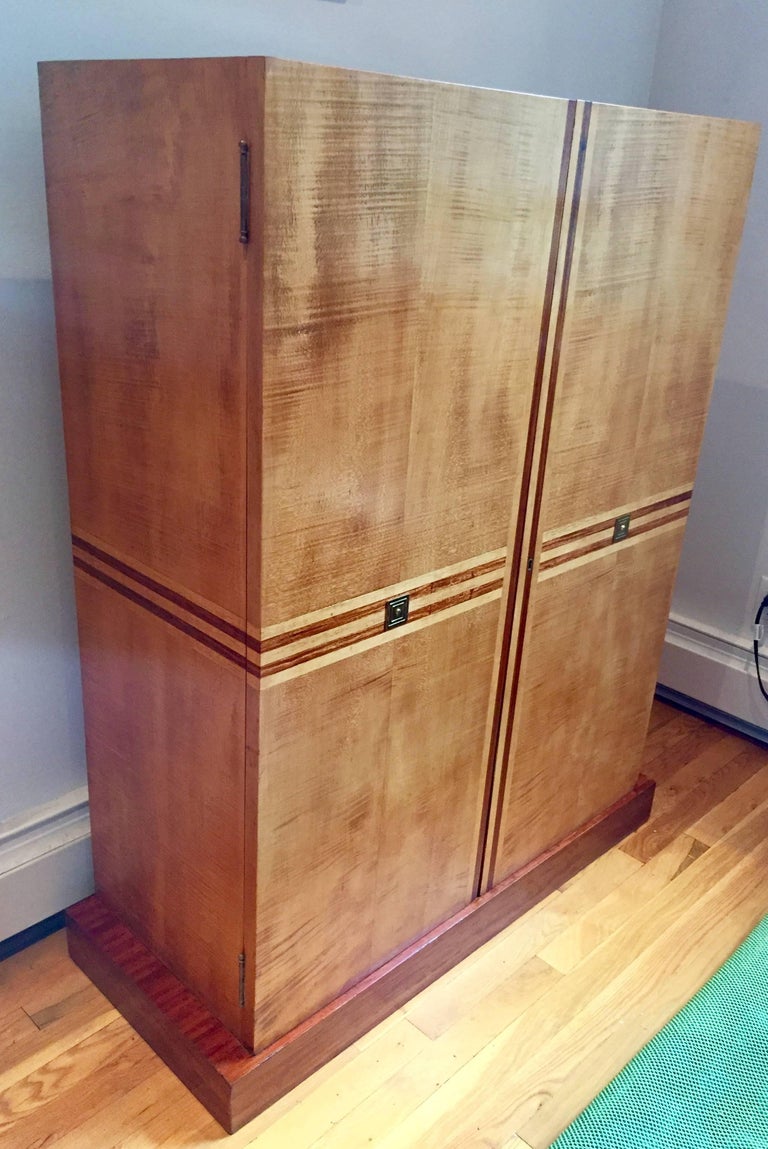 Figured birch cabinet on plinth with sexy mahogany inlay racing stripe. The interior is fitted with drawers and fixed shelves. Unsigned but from a Parzinger decorated Bergan County, NJ interior, circa 1950s.