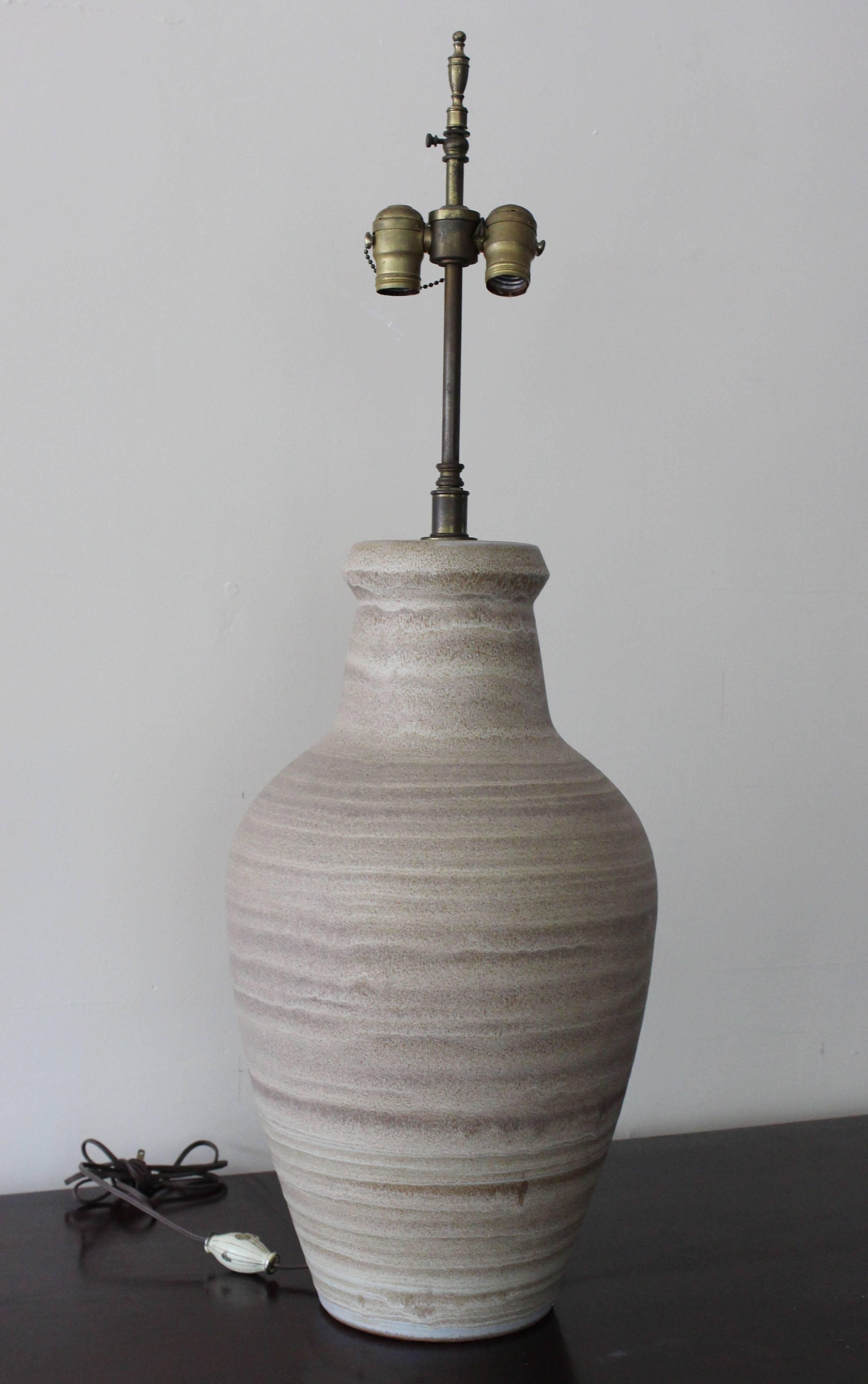 A large terra cotta lamp, matte glazed with earth tones; patinated brass hardware; double sockets and adjustable shade stem.

Base is 22.5 inches high.

        