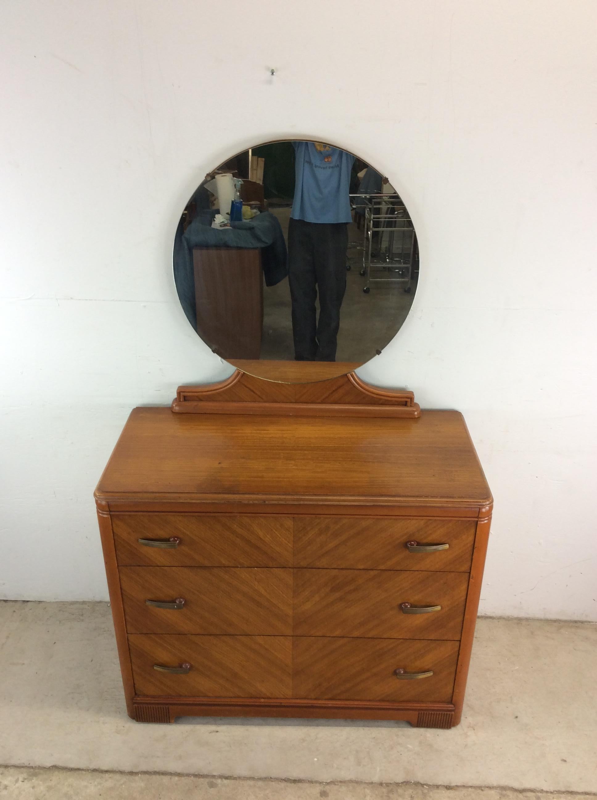 This antique Art Deco chest by Huntley Furniture features hardwood construction, beautiful veneer with original finish, three dovetailed drawers with brass & Bakelite hardware, and a mounted round mirror with wood base.  Mirror measures 32” tall