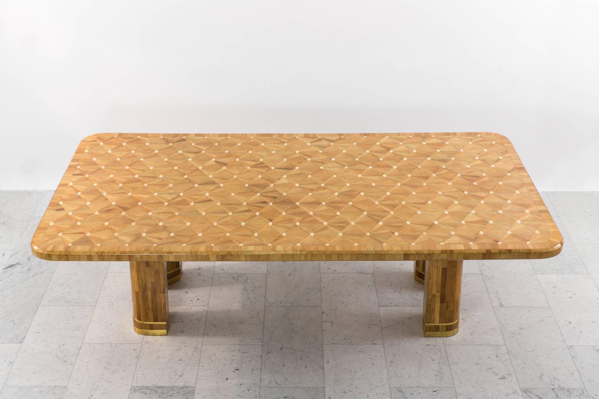 This magnificent table, executed in raffia wood marquetry, features a delicate bone inlay taking the form of fans across its lacquered surface. Standing on four uniquely shaped pentagonal plinths, the decorative border bottom is gilded in a 24-karat