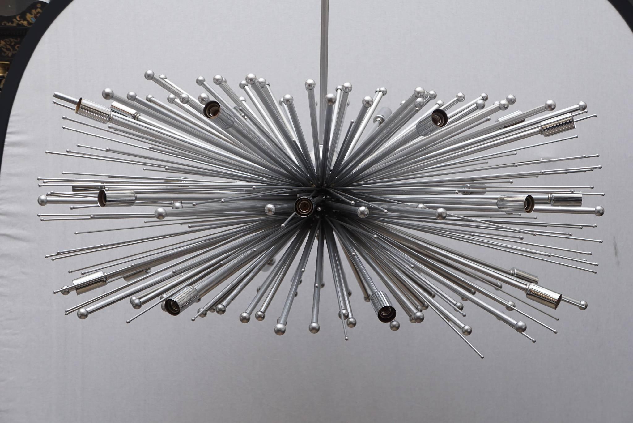A handmade chandelier made with steel and bronze by Lou Blass with a polished nickel finish and accents. These chandeliers are custom and made to order with a variety of sizes and finishes. This chandelier has 24 lights, and the maximum wattage per