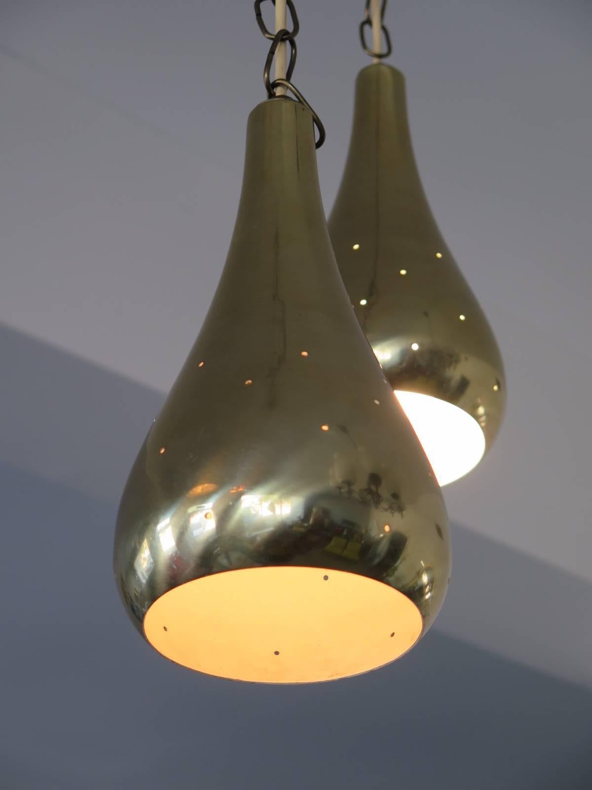 A pair of Paavo Tynell style pendant lamps. Polished brass, with perforations. Hourglass shape.