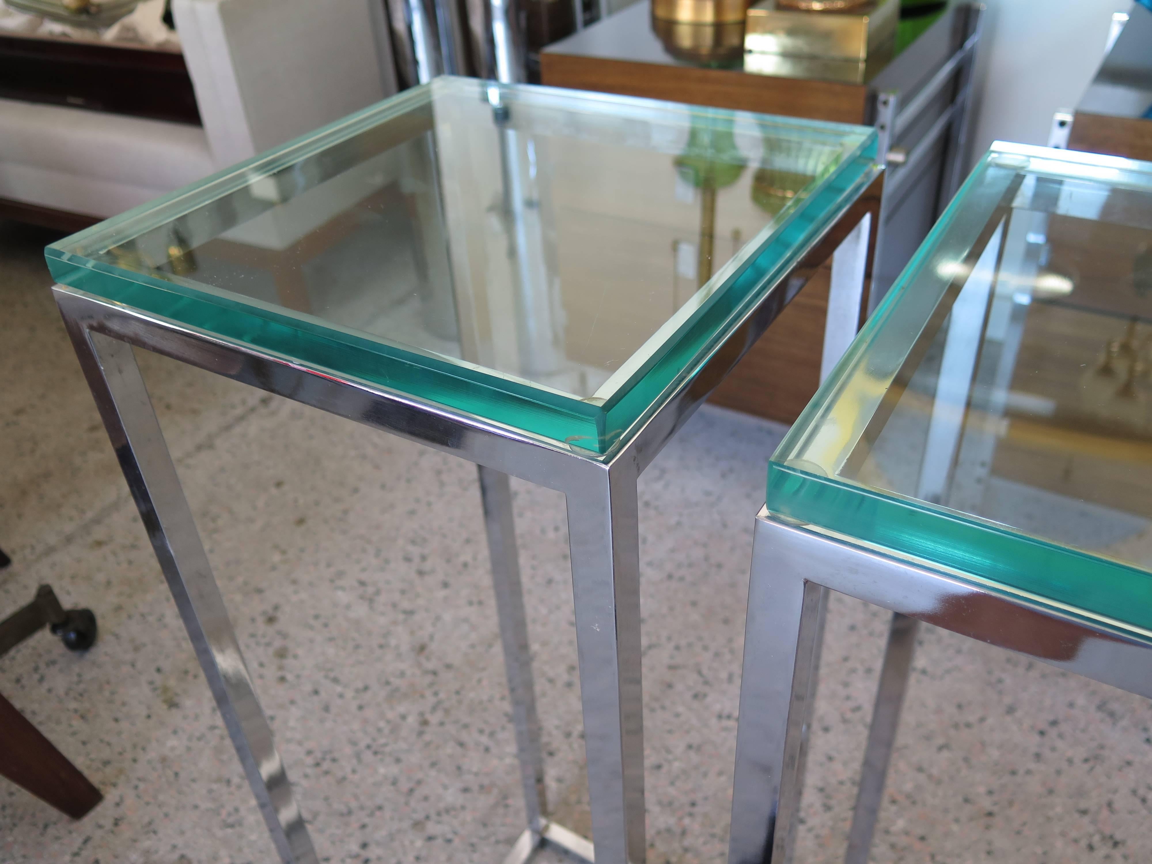 A pair of tall, chrome pedestal tables with glass tops. Chrome-plated brass frames, 3/4"bevelled glass. Measuring: 34.25" H, 12" D, 12" W.