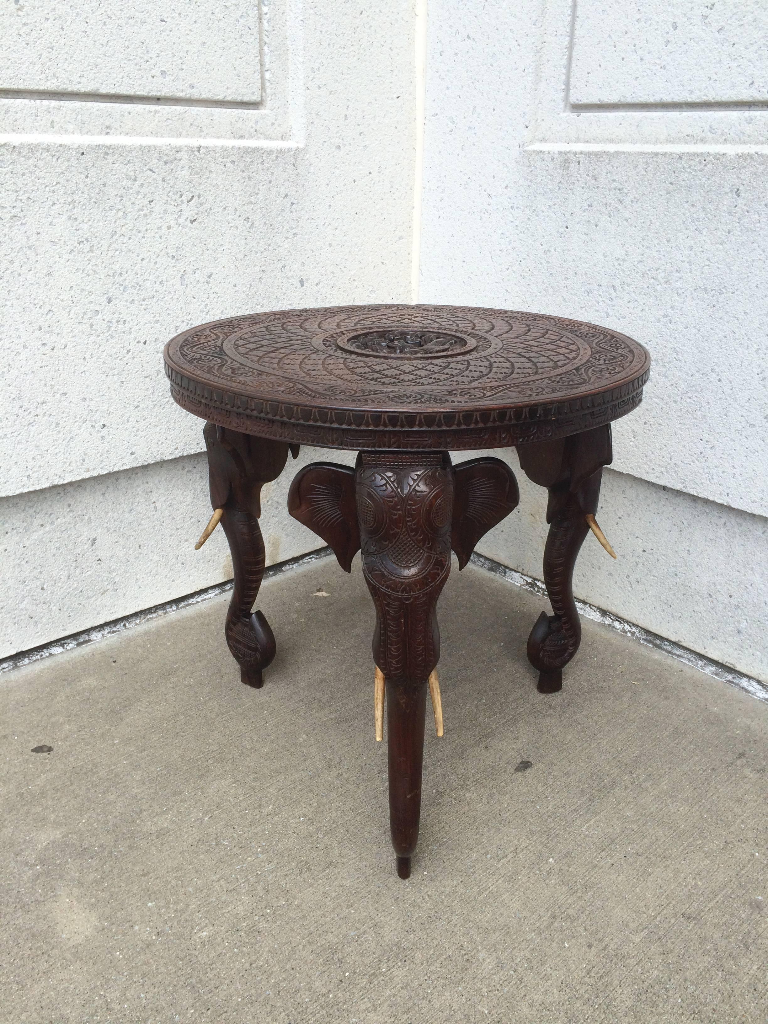 Intricately carved Anglo Indian rosewood side table with three elephant head supports, each shown holding a perfume bottle in the curve of the trunk, all with faux tusks. The center medallion of the top showing a Hindu Goddess seated in lotus