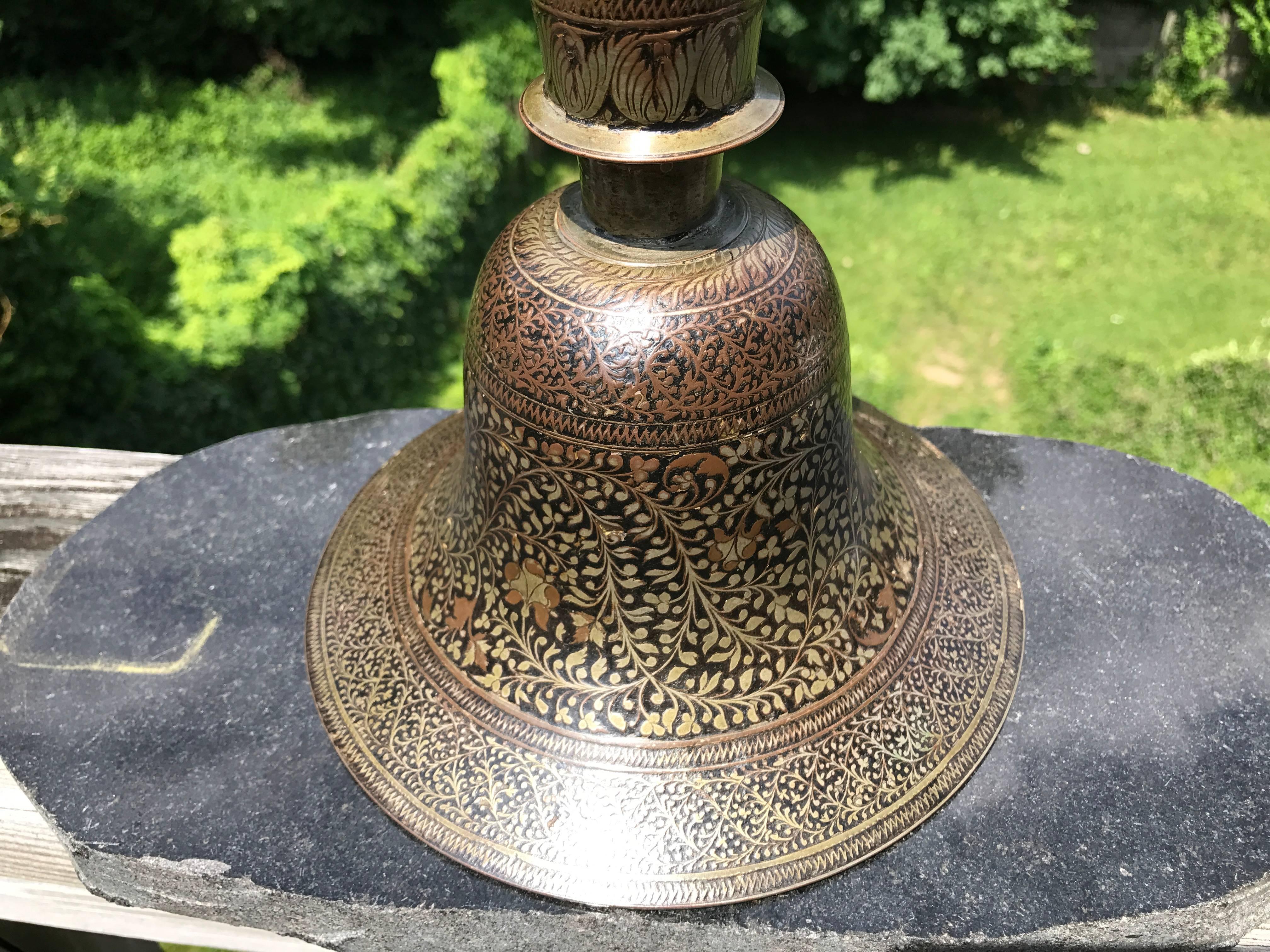 This hookah base of elegant bell form, with a round, flared neck with a collar is decorated overall with an intricate floral pattern in inlaid silver and brown and black lacquer. 
A huqqa or hookah is a traditional water pipe, smoking instrument