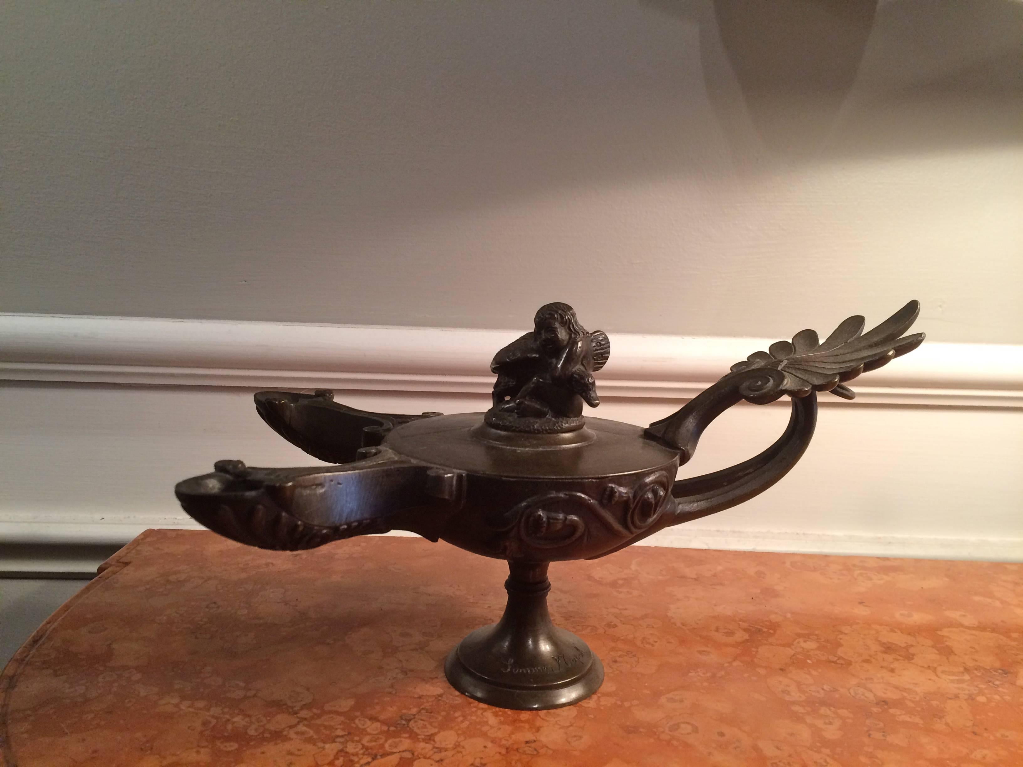 Italian 'Grand Tour' bronze oil lamp, after the ancient Roman original, with two spouts and removable top depicting Cupid wrestling the swan. Acanthus leaf handle, signed Sommer, Napoli. 
The Fonderia Sommer was one of the two top foundries casting