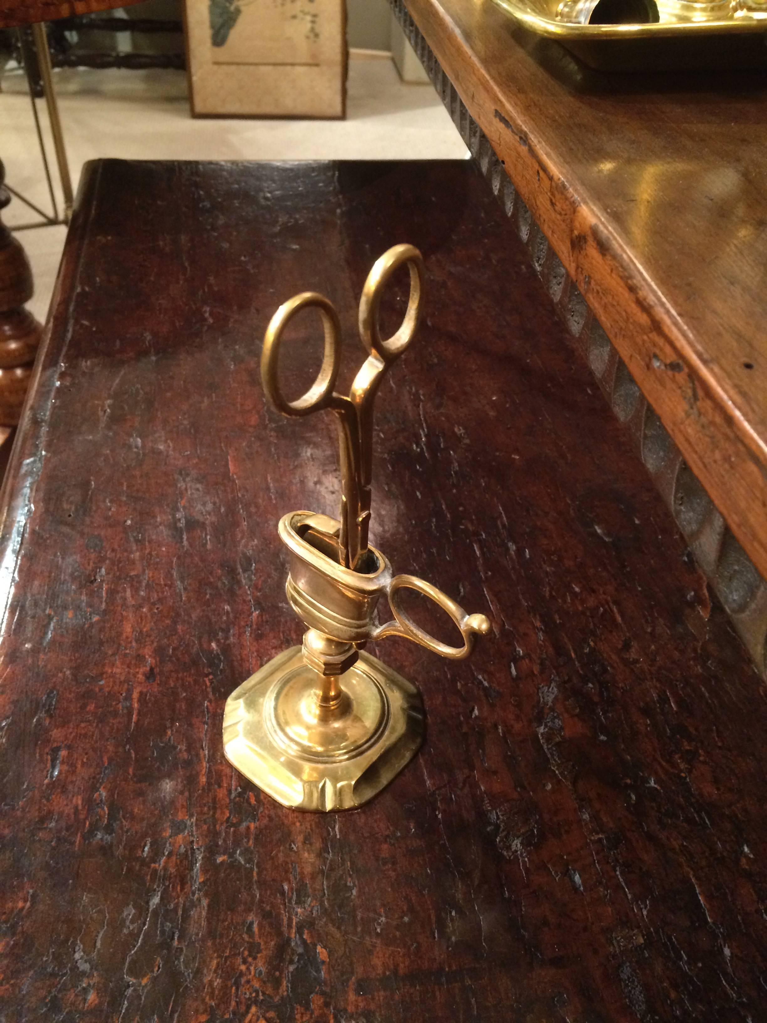 An English Queen Ann style brass candle snuffer with scissor-like handles and a pointed tip, which is accommodated vertically into the stand. With an octagonal based stand with a shaped handle. There are two holes in the bottom of the stand so that
