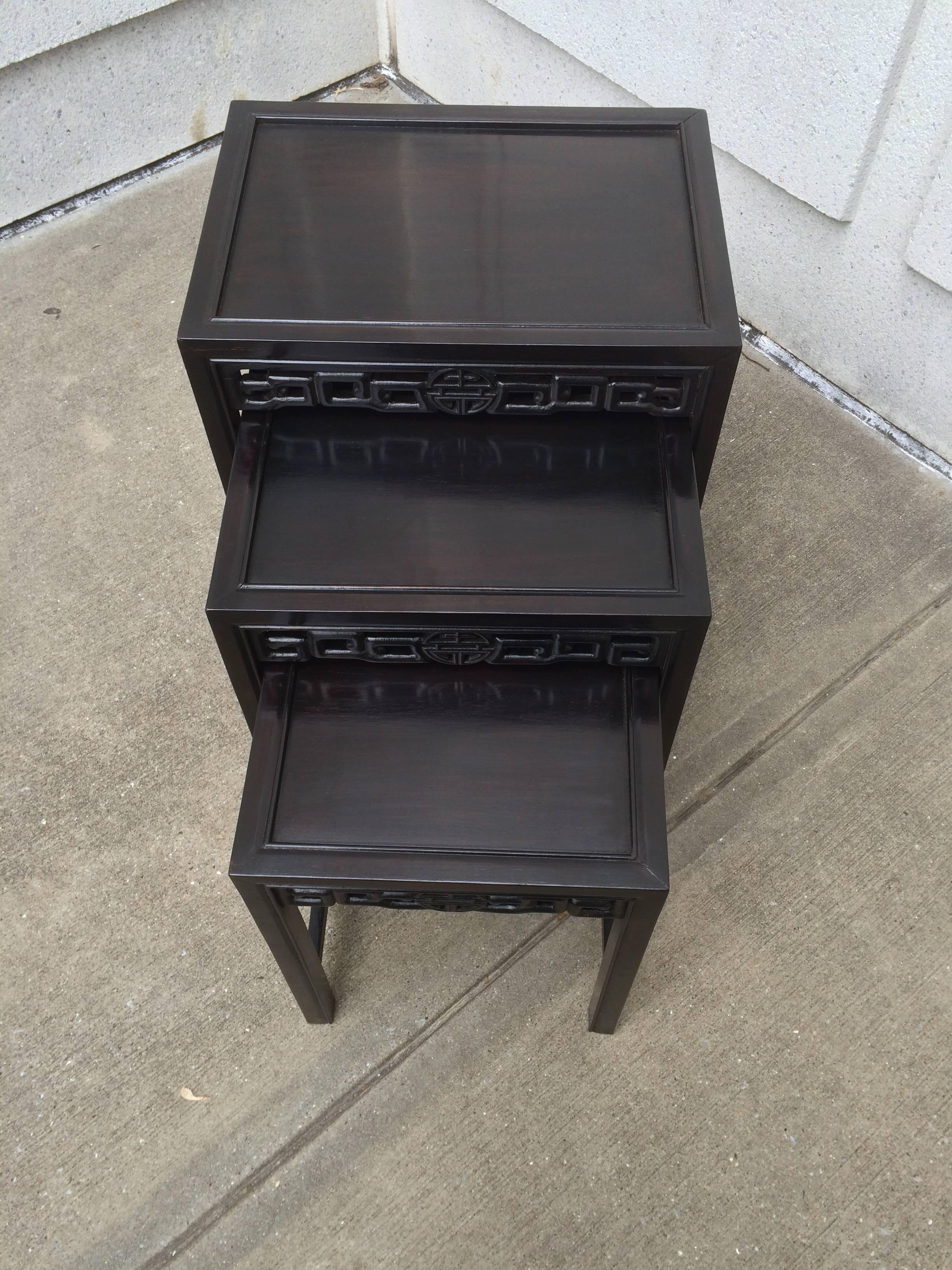 Set of three Chinese nesting tables, carved of hard wood with a rich ebonized finish with reddish undertones. Each with a carved openwork apron. The tables fit together as one or come apart as three separate tables. Great for entertaining.