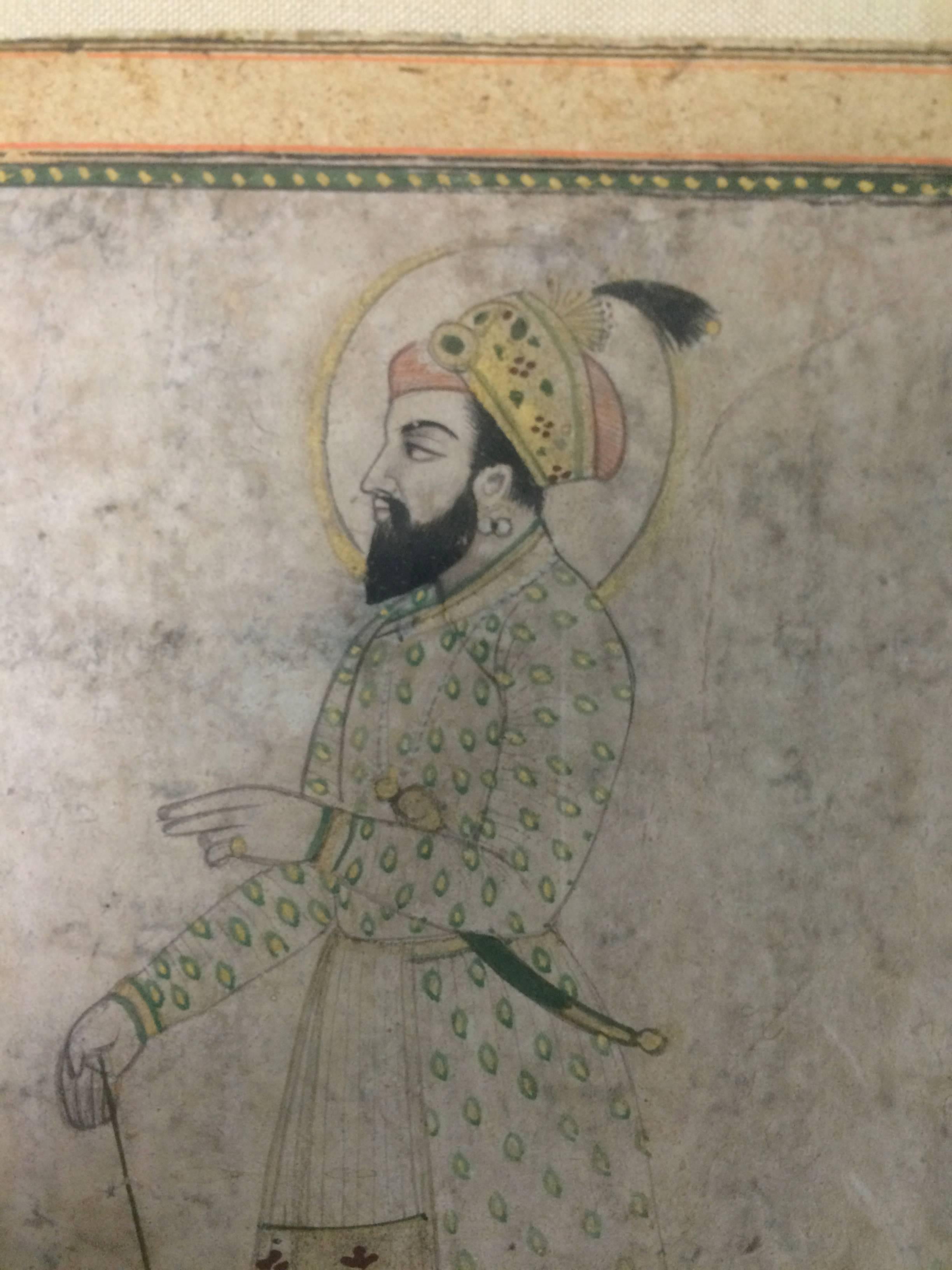 Portrait of a Mughal Prince or nobleman painted in watercolor and ink on paper.  The Prince shown standing, wearing a green gown with an embroidered apron, cap and silk slippers, earrings and a gold ring, holding a cane, a kris type dagger tucked