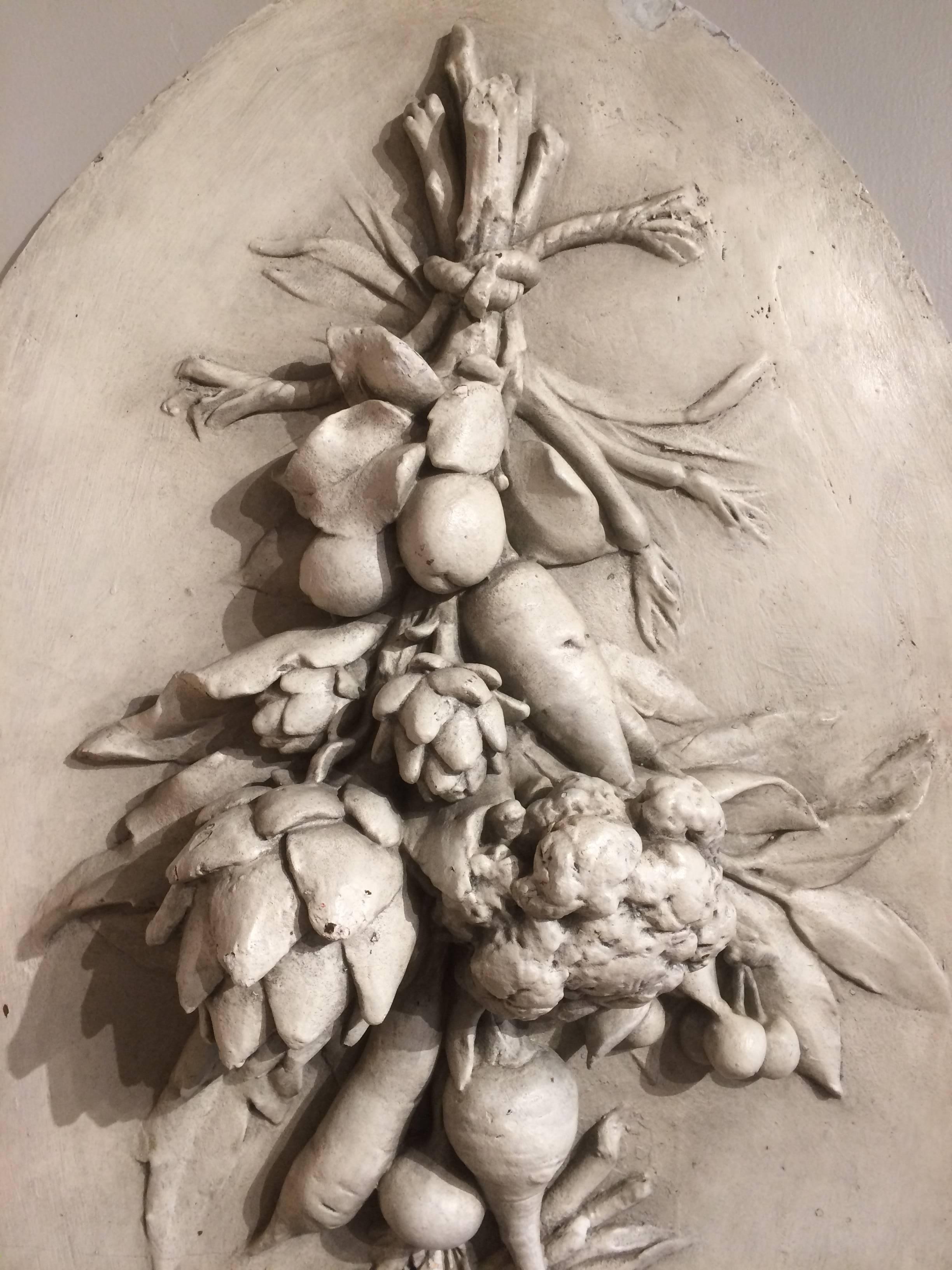 A 19th century French plaster oval medallion with artichokes, cauliflower, scallions, various root vegetables, grains and legumes shown bound together and hanging from a wall. In deep relief, a very compelling wall sculpture, perfect decoration for