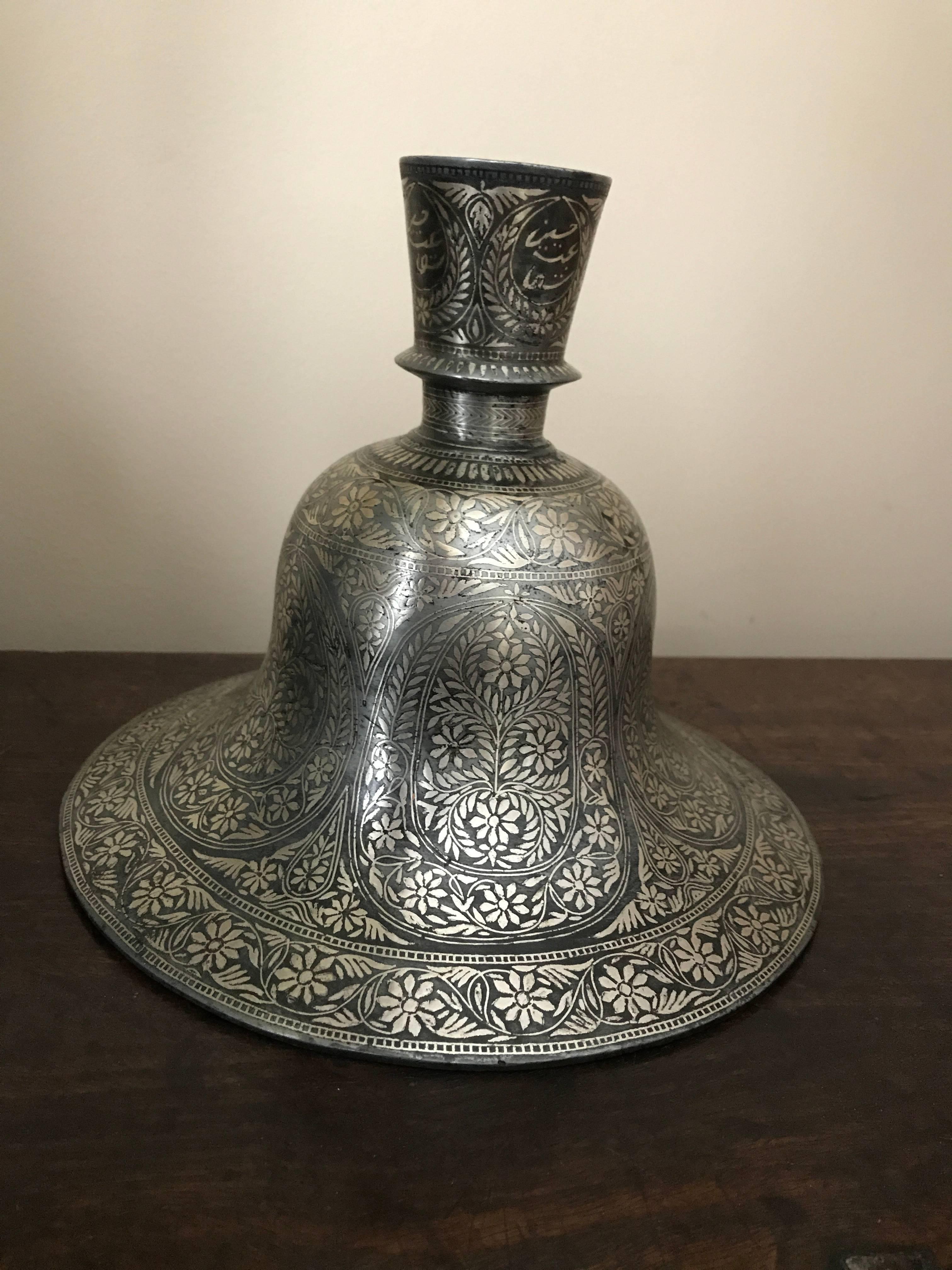 This bidri hookah base is cast in an elegant bell form, with a round, flared neck with a collar, and is decorated overall with an intricate floral pattern in inlaid silver. A huqqa or hookah is a traditional water pipe, smoking instrument