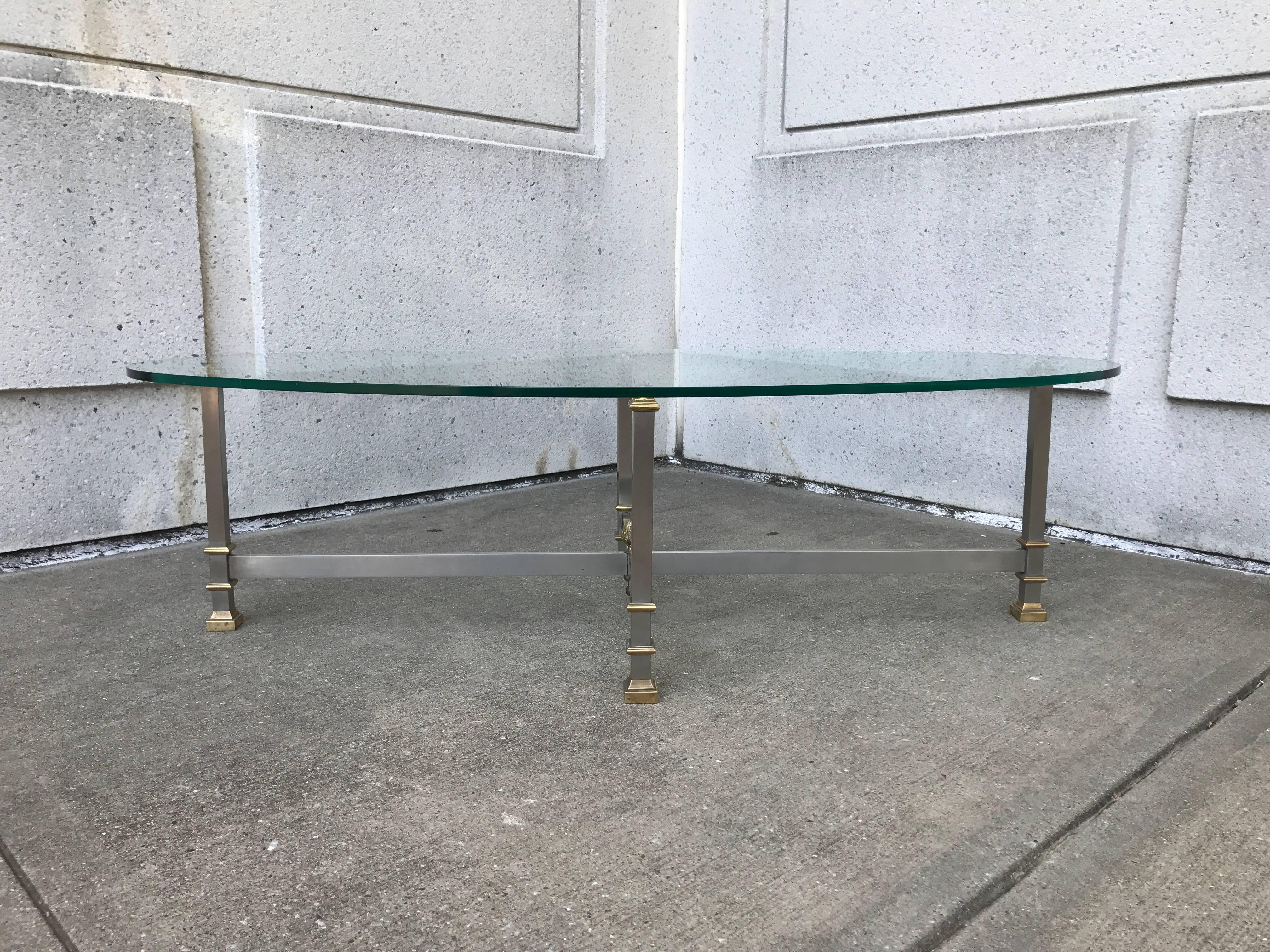 Unusual Maison Jansen style steel and bronze oval shaped glass topped coffee table with X-form base. With four neoclassical style geometric column legs, the cross stretchers joined by an artichoke finial.
