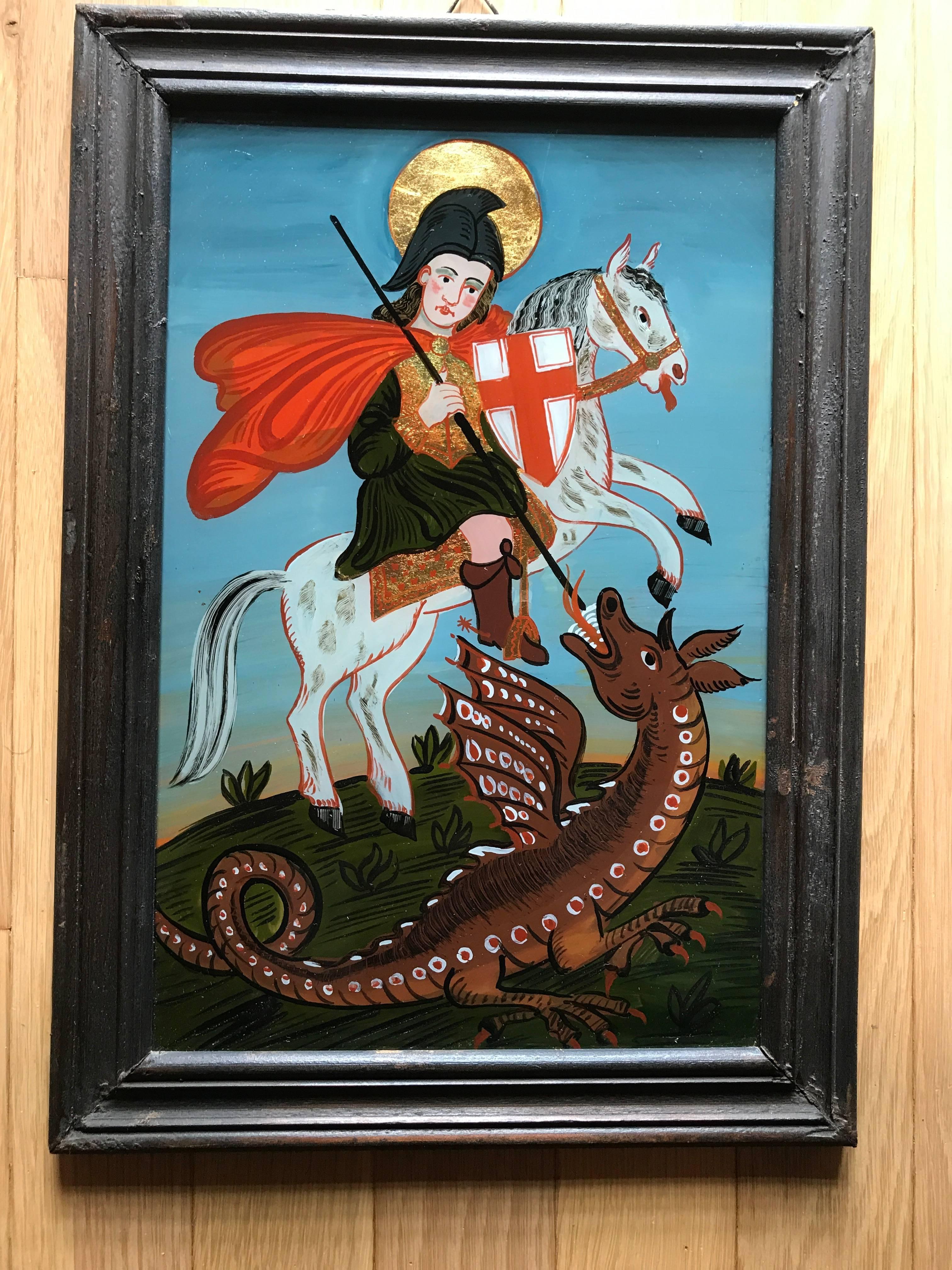 Verre églomisé, or reverse glass painting with gilding of Saint George and the Dragon. St George shown riding his steed, slaying the dragon with his spear. In a period black painted frame. The wonderful aspect of reverse glass painting is the