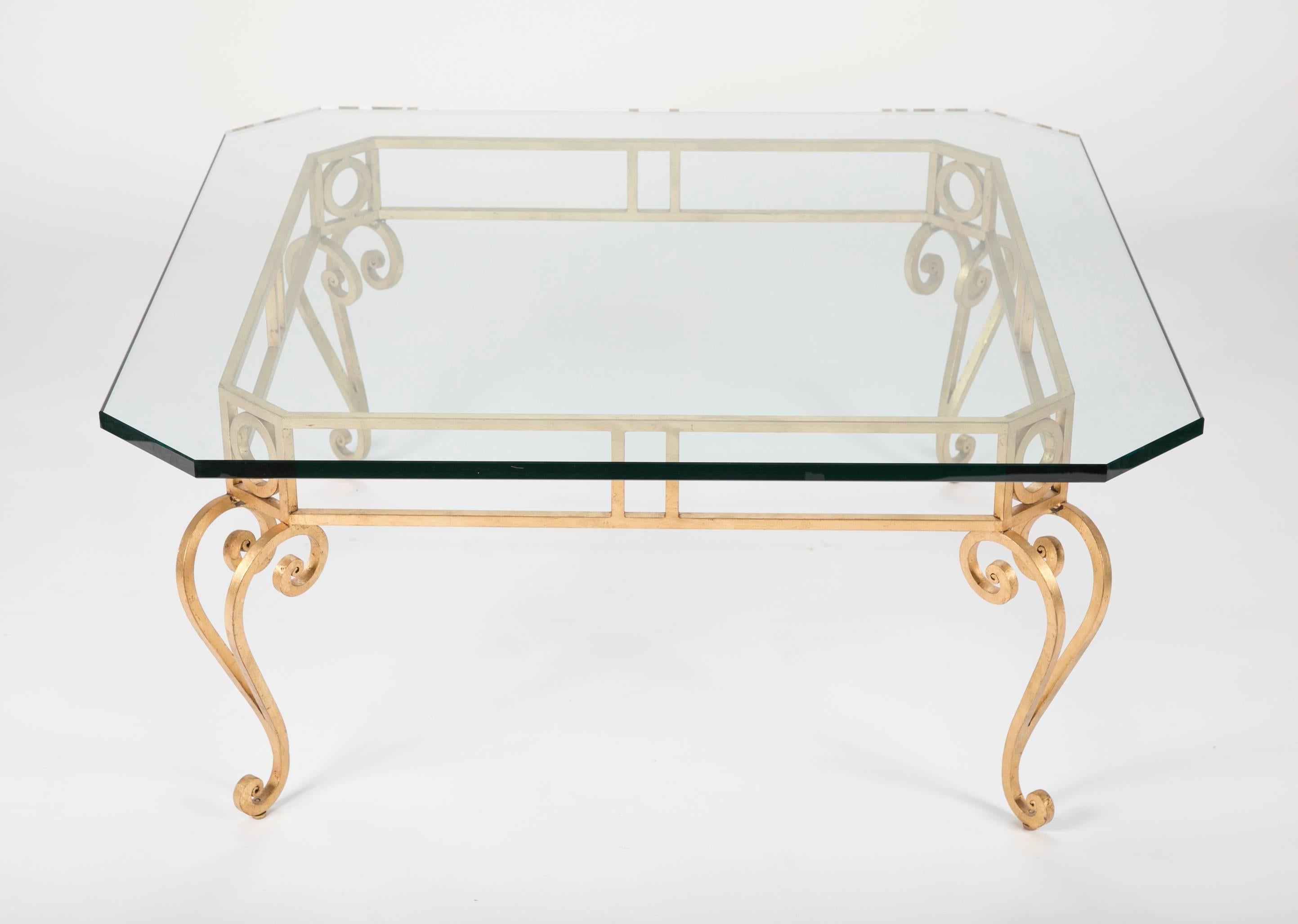 Table basse moderne du milieu du siècle dernier avec un épais plateau en verre carré à coins coupés sur une base en fer forgé doré avec des pieds en cabriole. Reprenant avec chic le style Louis XV, cette table présente de belles lignes, à la fois