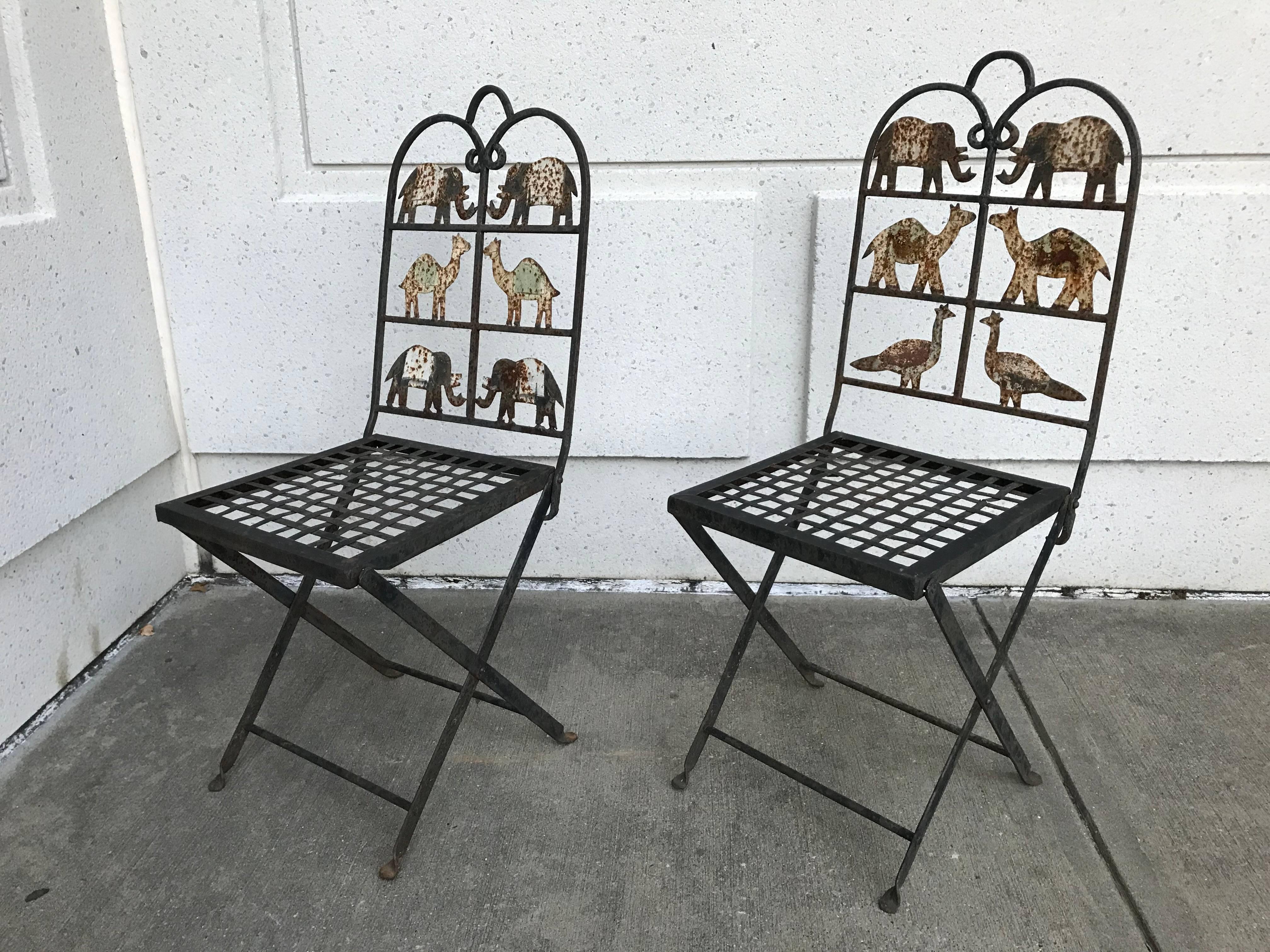A whimsical pair of wrought iron folding garden chairs with painted animal cutouts, including elephants, camels and peacocks. These chairs are utterly charming, the weathering of the surface only adding to their appeal. They do fold and are suitable