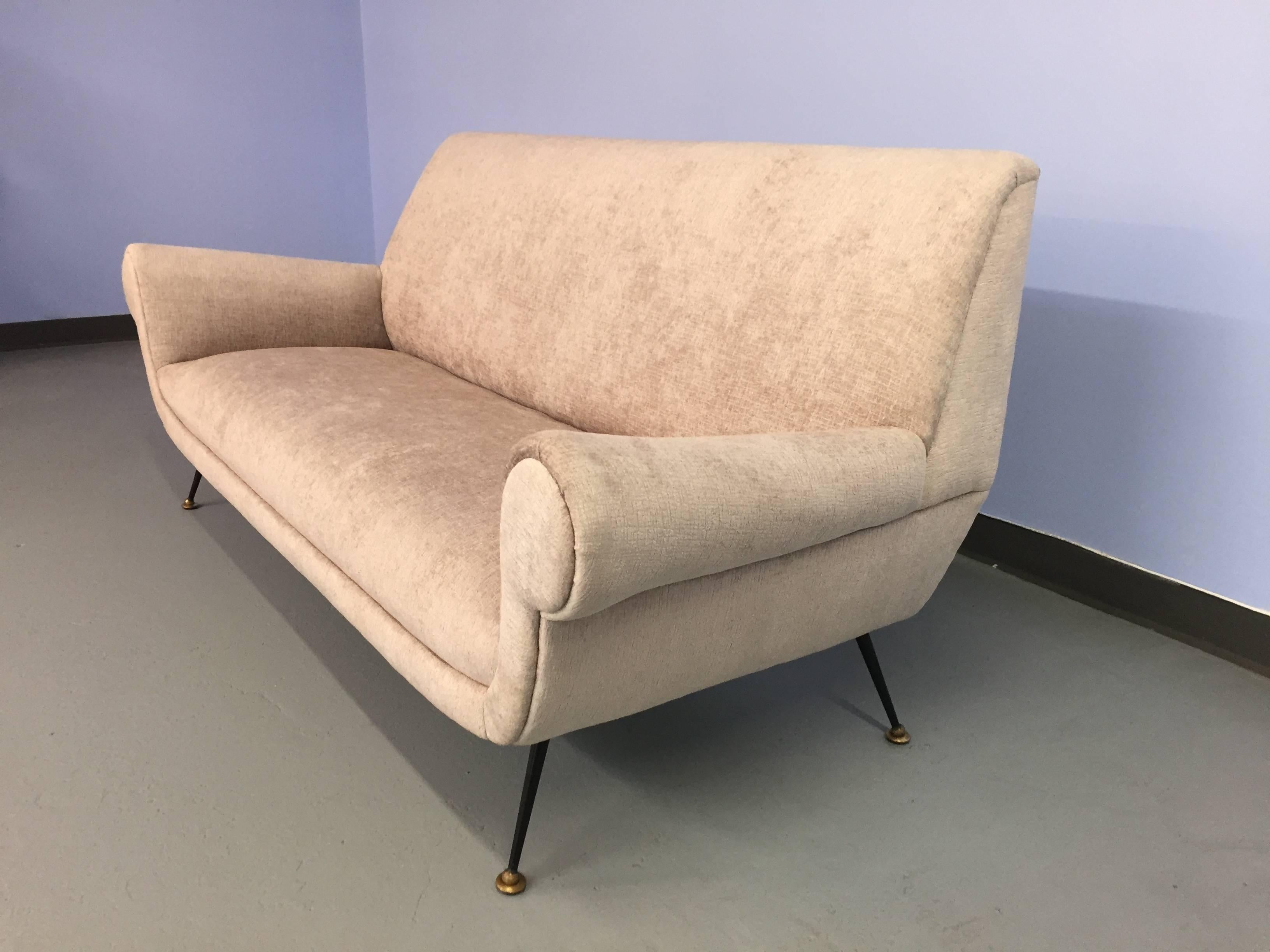 Newly upholstered in light grey velour with cross-hatched patterning. The side profile of this sofa is particularly striking, with sharp, angular lines. Other details include the distinctive legs, teared and black, tipped in brass ball and plate.