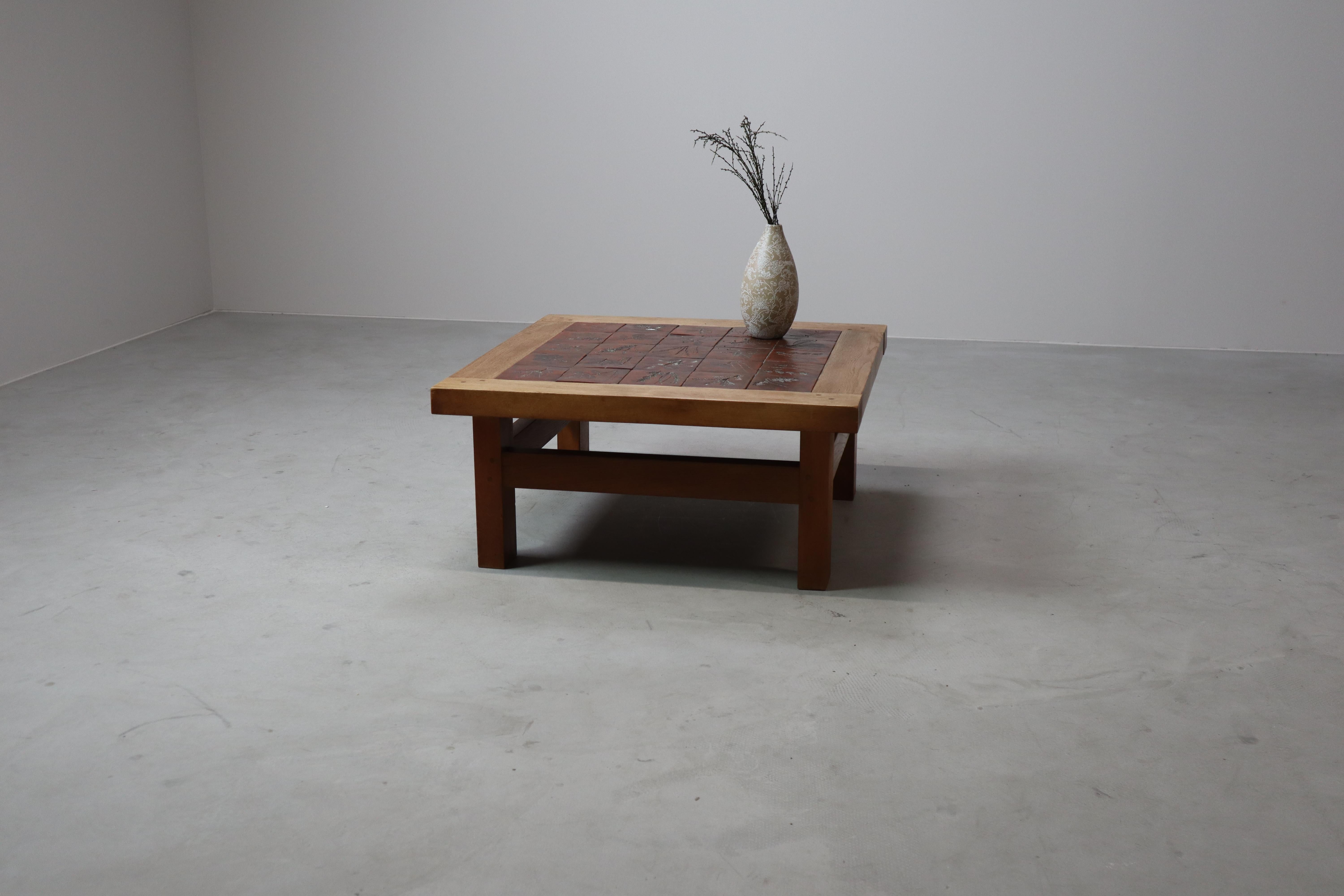 This handcrafted mid-century coffee table features a striking square top composed of 25 ceramic tiles, each uniquely decorated with pressed botanical motifs – including leaves, stems and foliage – evocative of nature’s delicate imprint. The