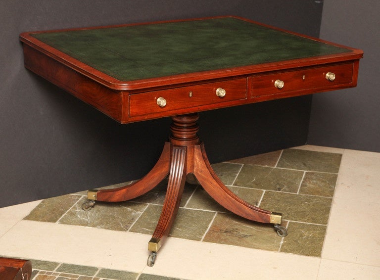 A Regency mahogany pedestal library or gaming table with inset leather top, the frieze fitted with two drawers and raised on a turned pedestal with quatropod supports ending in brass casters.