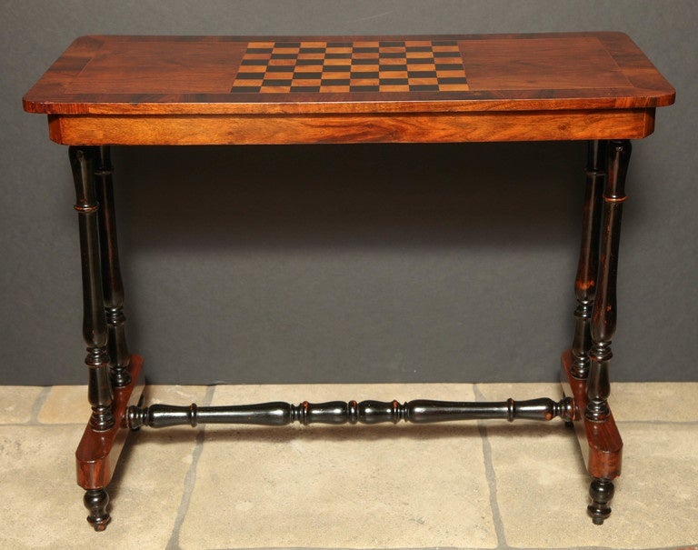 A Regency rosewood trestle-end game table, the rectangular cross-banded top centering an inset satinwood and ebonized checkerboard, on ebonized turned trestle supports and with conformingly turned stretcher base.