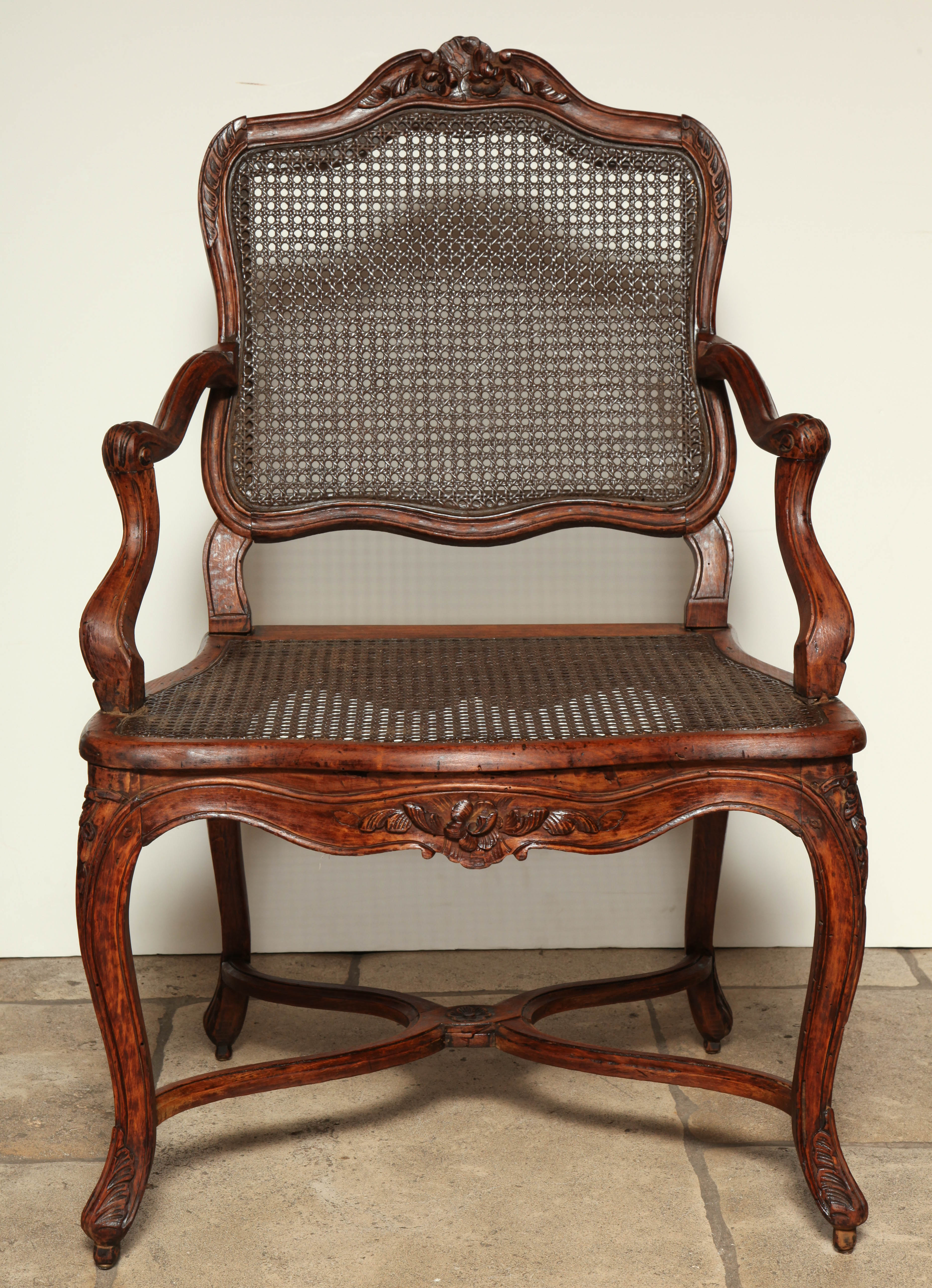 Pair of Regence carved and stained beech cane-filled fauteuils with cartouche shaped backs, scrolled arms and X-form stretchers.